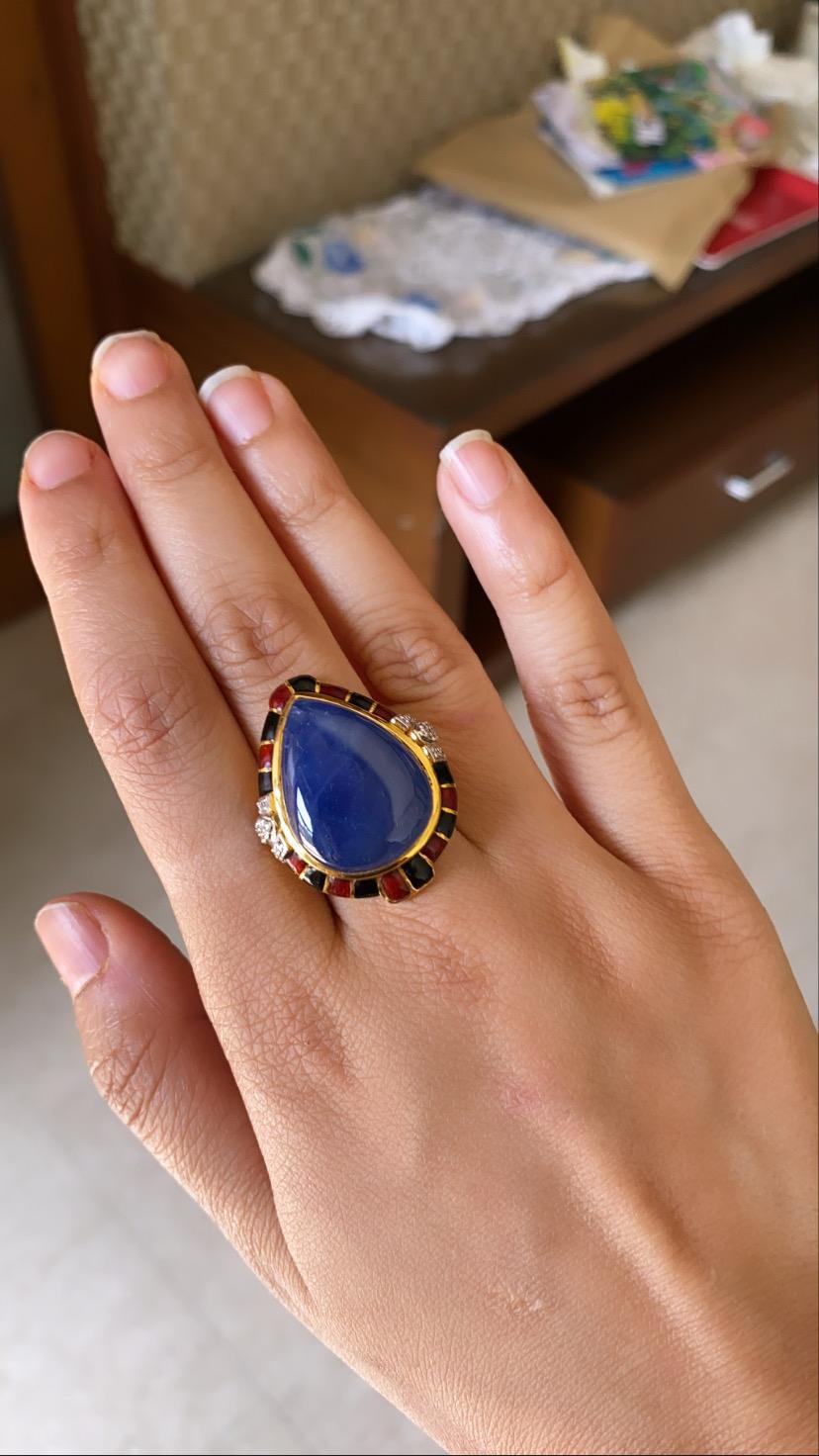 A modern enamel ring set in 18k yellow gold with black and red enamel and natural blue sapphire cabochon. The blue sapphire is natural and originates from Burma and weight approx 35.76 carats, diamond weight is .16 carats . The net gold weight is