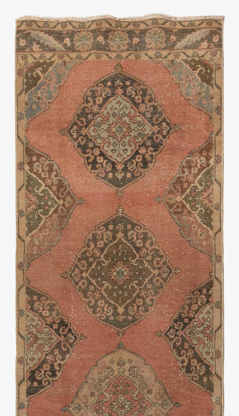 A vintage Turkish runner rug in red, brown red and beige colors. It was hand-knotted in the 1960s with low wool on cotton foundation and features a multiple medallion design. It is in very good condition, professionally-washed, sturdy and suitable