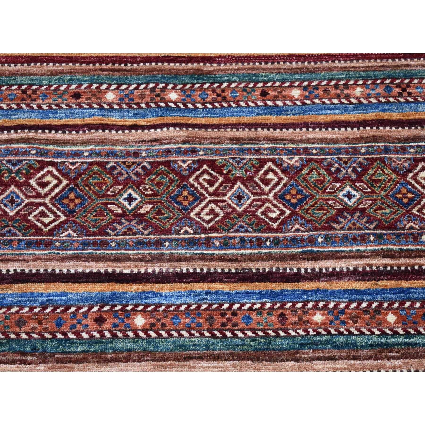 Se trata de una auténtica alfombra oriental de color rojo intenso, anudada a mano en pura lana, afgana Super Kazak con tintes naturales y diseño Khorjin. Ha sido anudada durante meses y meses con técnicas artesanales de tejido centenarias por