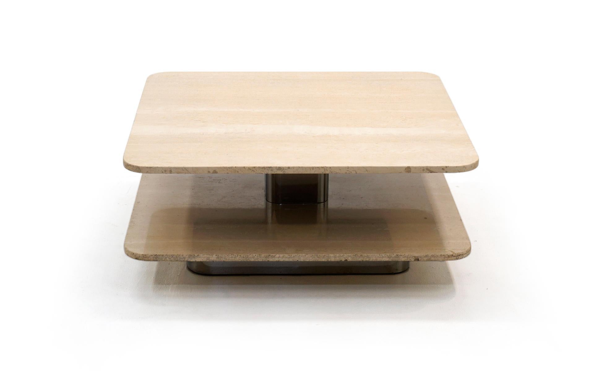 Two-tier square, with rounded corners, travertine coffee table. The lower travertine portion is secured to a recessed chrome base. That structure continues through the center of the travertine with a chromed steel support further recessed giving the