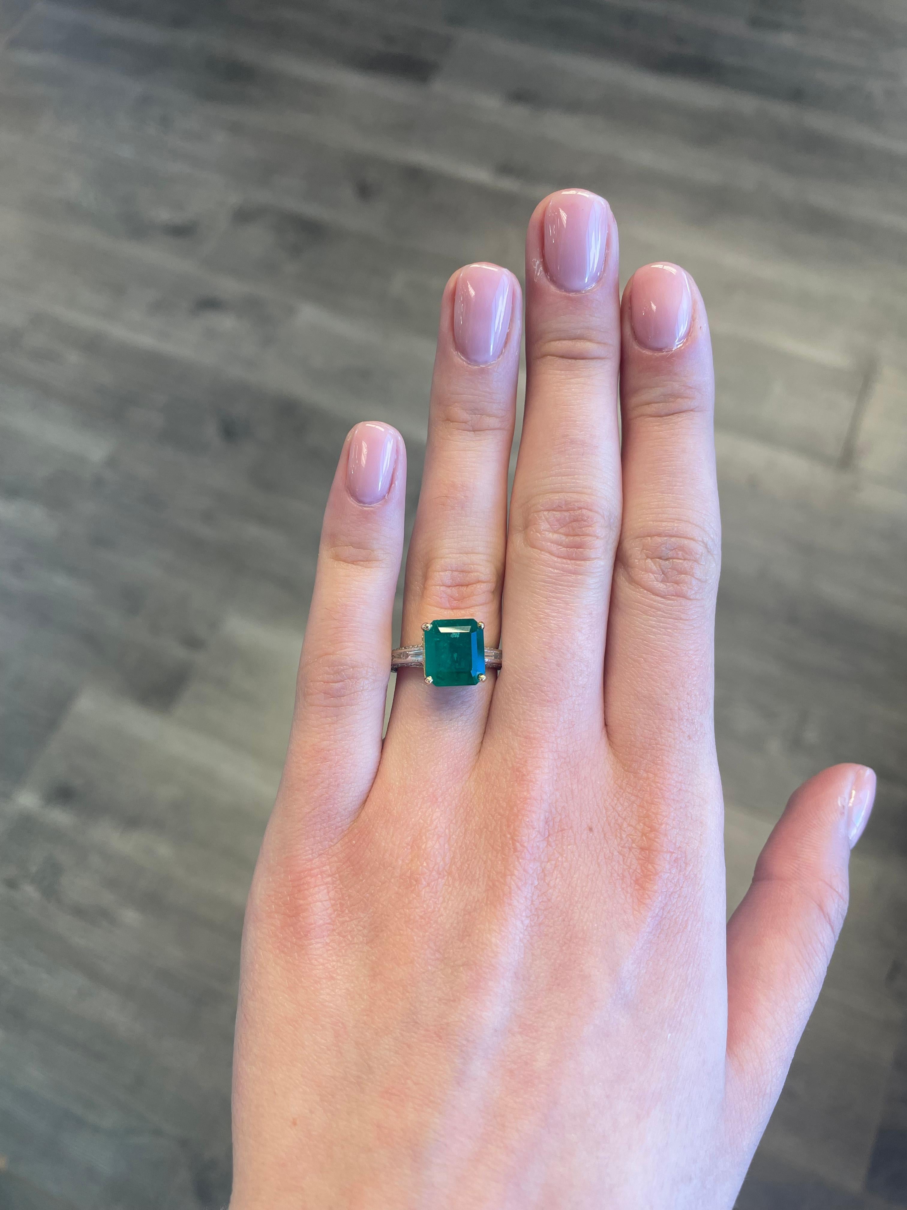 Atemberaubender moderner Smaragd- und Diamant-Halo-Ring mit geteiltem Schaft.
3.64 Karat Smaragd im Smaragdschliff, ca. F2. Ergänzt durch Diamanten im Baguetteschliff und im Rundschliff. Ungefähr G/H Farbe und SI Klarheit. 18 Karat Gelbgold und
