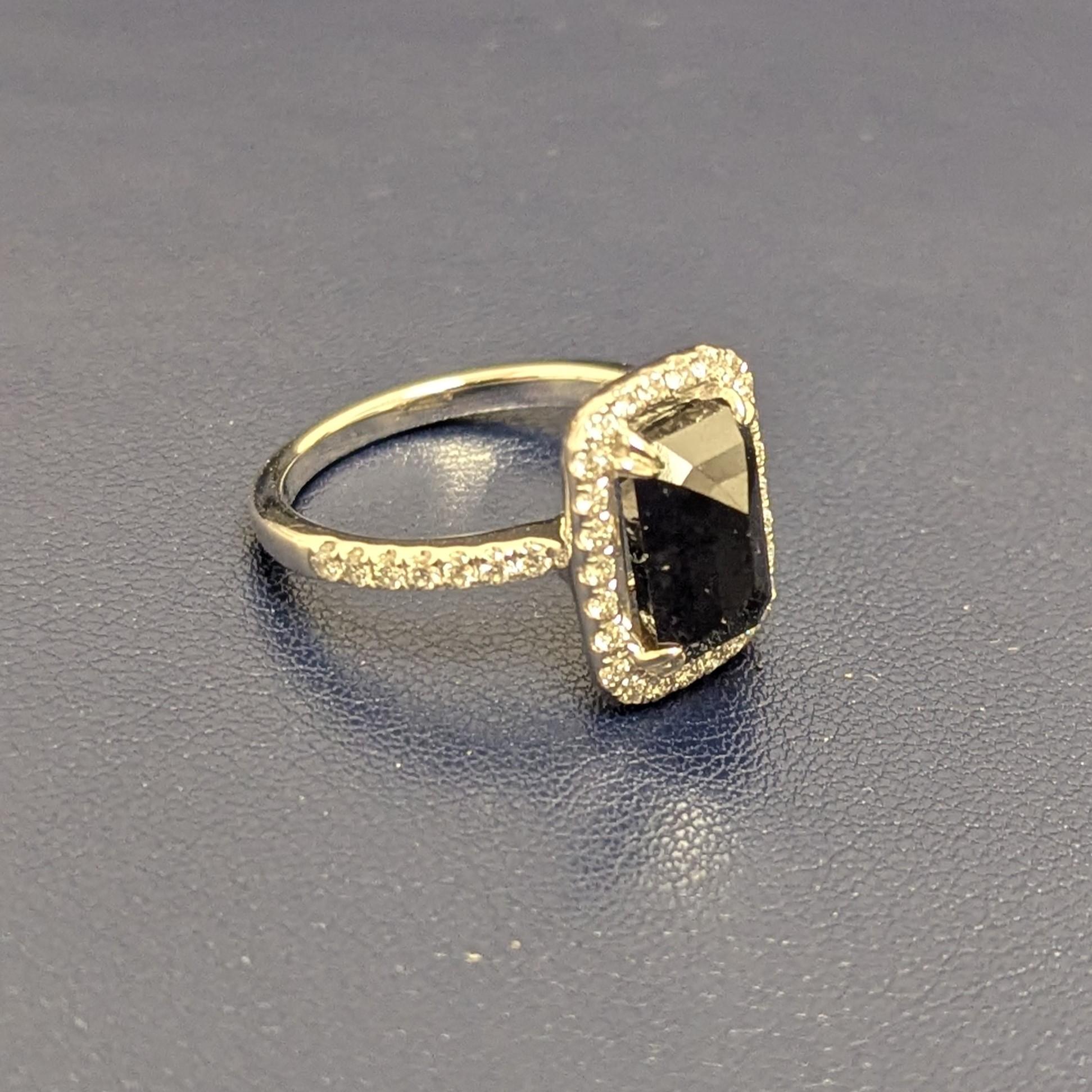 This ring features a bold, black diamond, weighing approximately 3.65 carats, that is cut-corner, rectangular, step-cut, reverse-set and surrounded by round brilliant-cut diamonds and diamond-set shoulders, meticulously mounted in 18K white gold.