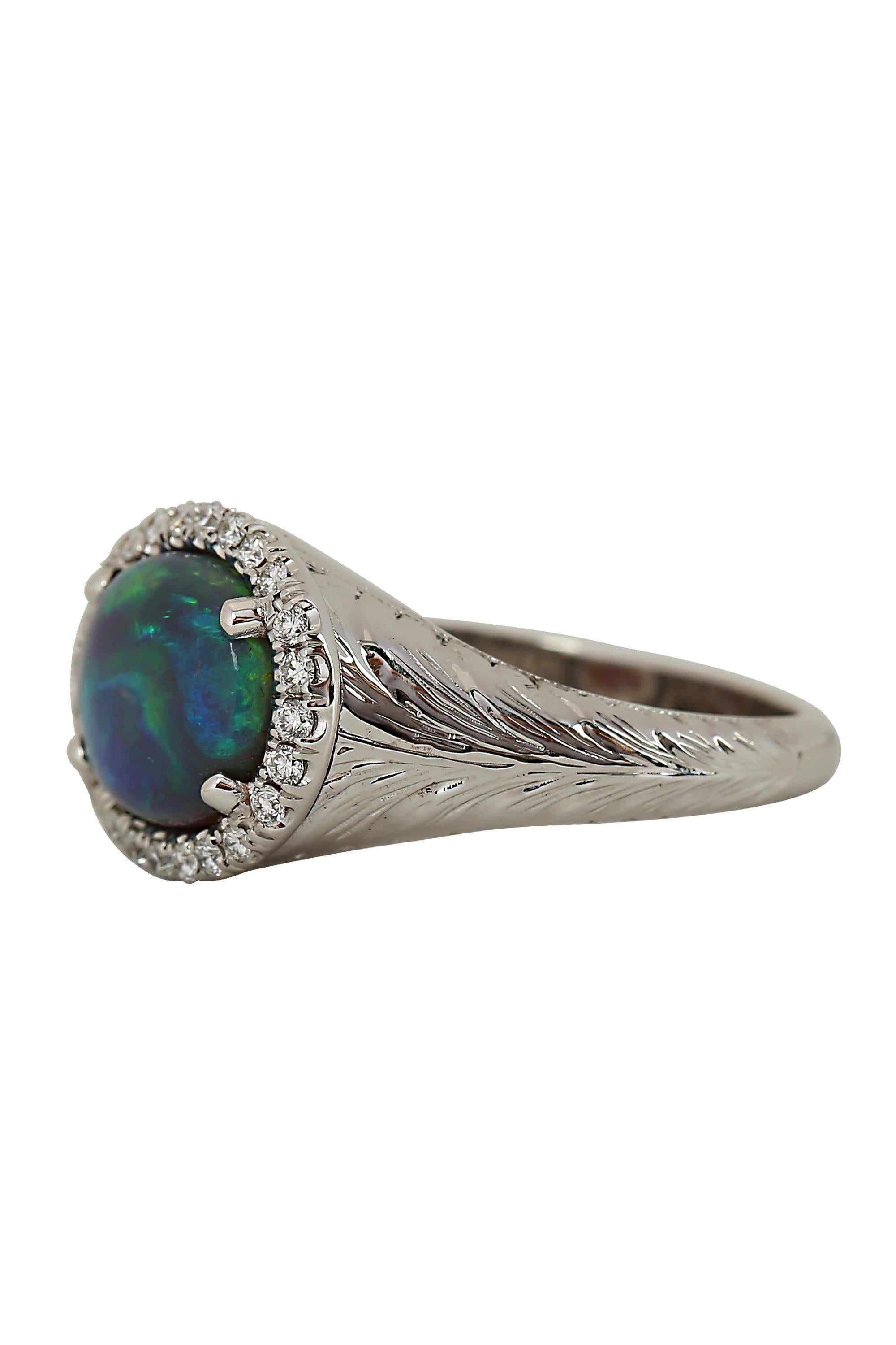 An opal and diamond ring featuring a 3.65 carat black opal displaying a beautiful tapestry of luminous green and blue hues emanating from a halo of bright white round brilliant diamonds. Completed by a finely crafted and subtly designed 18 karat