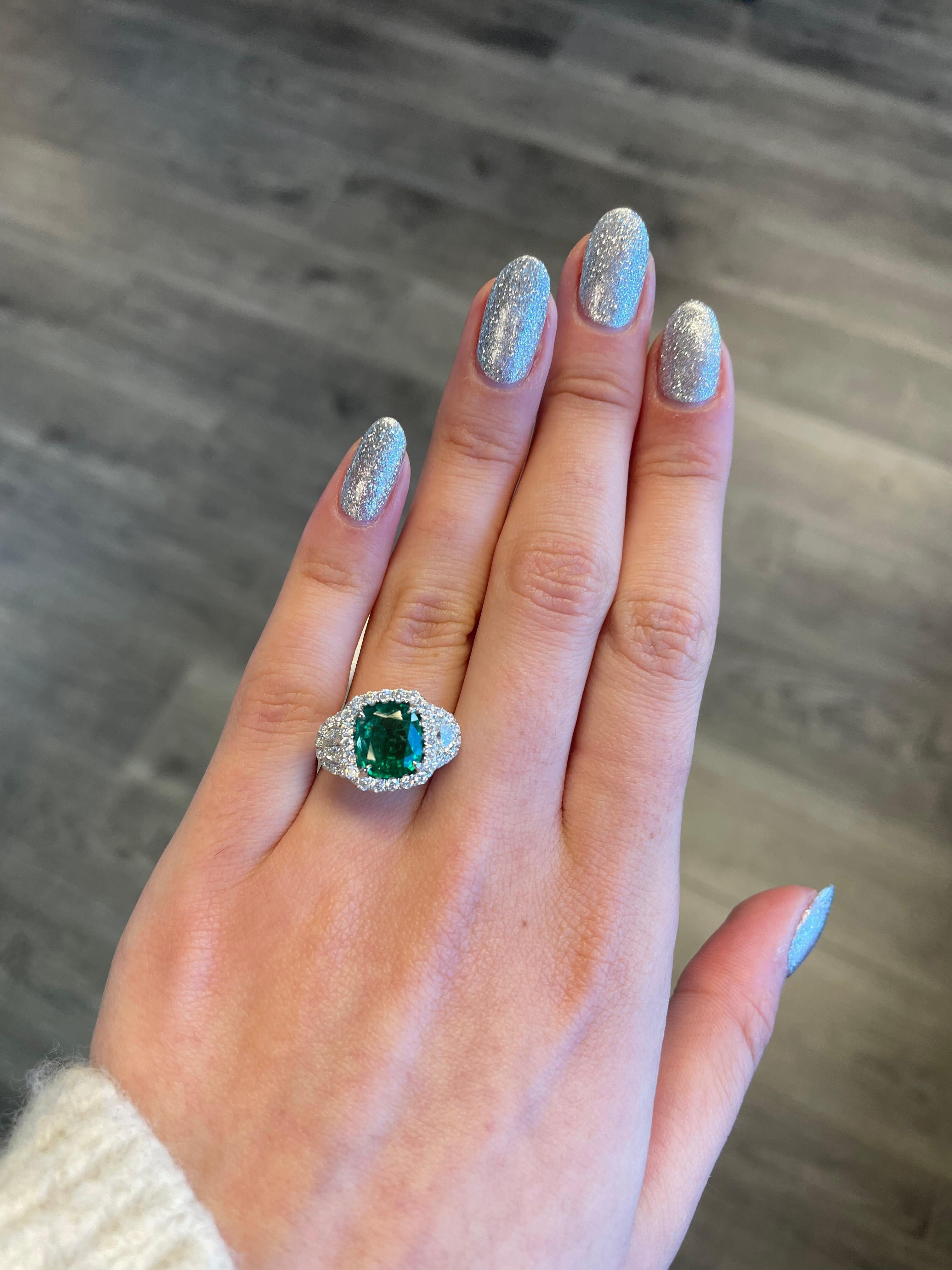 Stunning emerald and diamond three stone ring with halo.
3.67 carats total gemstone weight.
2.43 carat cushion emerald, apx F2. 2 half moons with 50 round brilliant diamonds, 1.24 carats. Approximately G/H color and VS-SI clarity. 18k white gold,