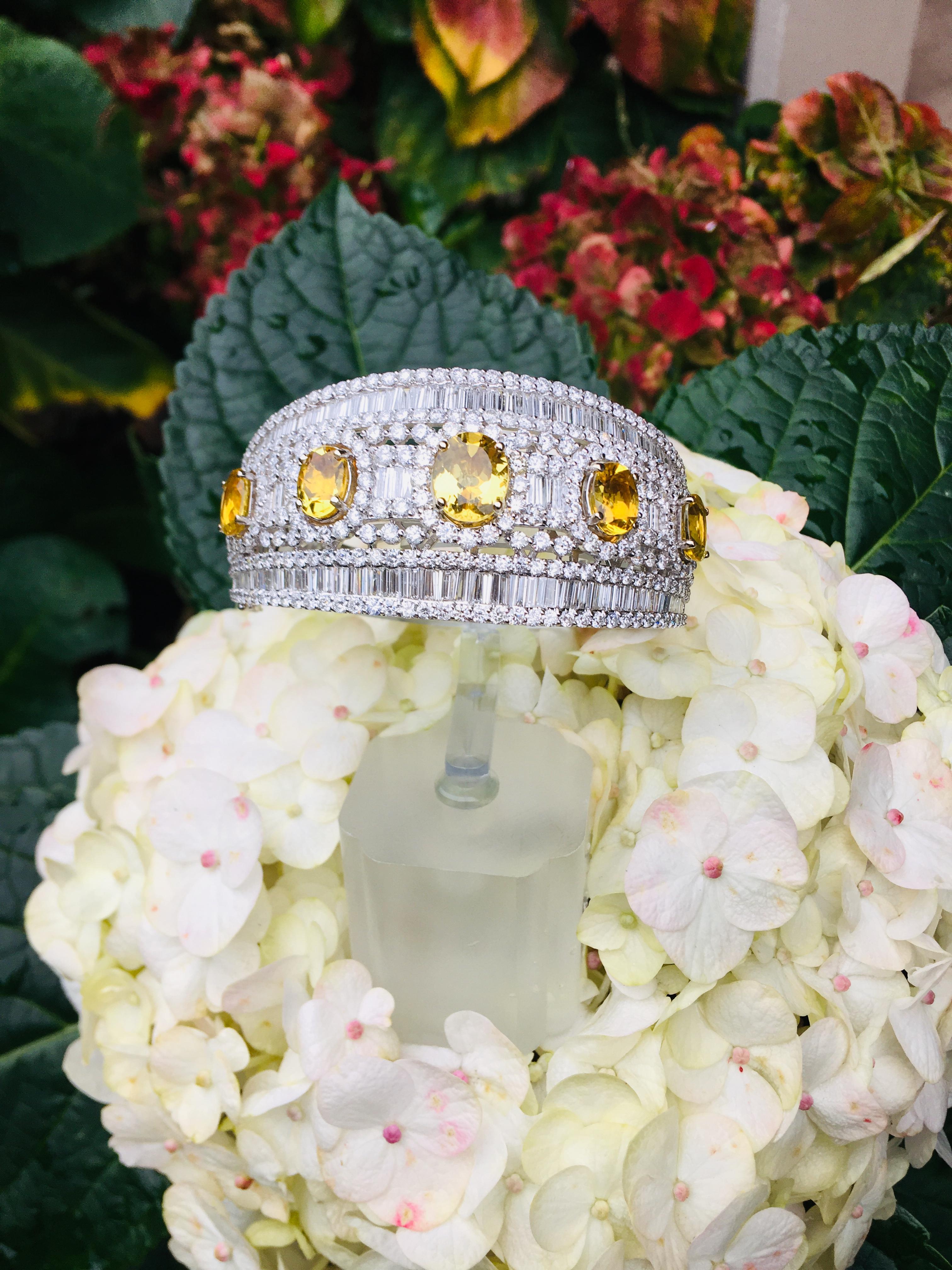 Incredible 18 karat white gold hinged, wide tapered bangle estate bracelet features approximately 28 carats of invisibly set diamond baguettes and prong set round brilliant diamonds, accented by 5 prong set, oval cut yellow topazes weighing