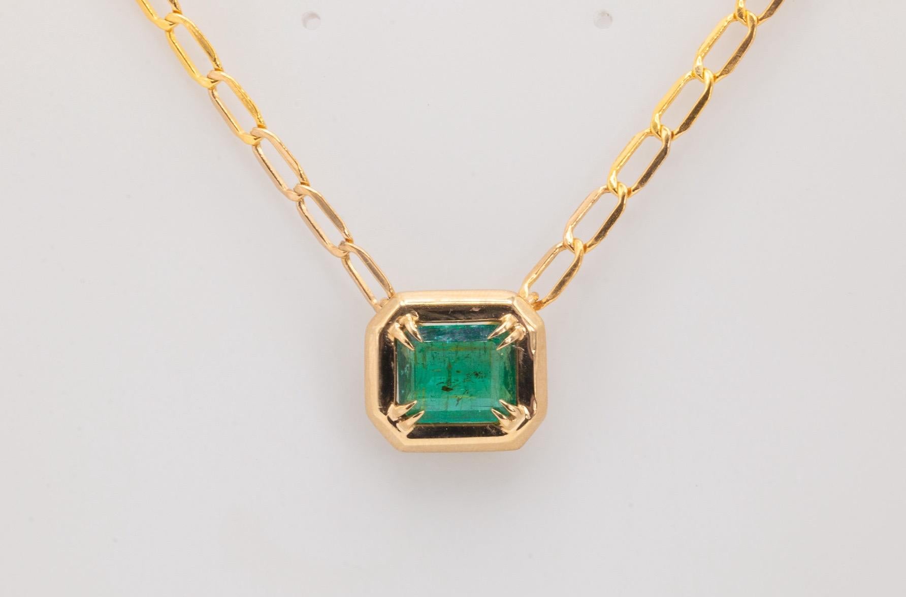This unique handmade bezel-set pendant features a stunning 3.7-carat emerald-cut Zambian green emerald, elegantly crafted in 14K yellow gold. The pendant measures 13.8mm in height and 25.4mm in width, creating a bold yet refined look. It is paired