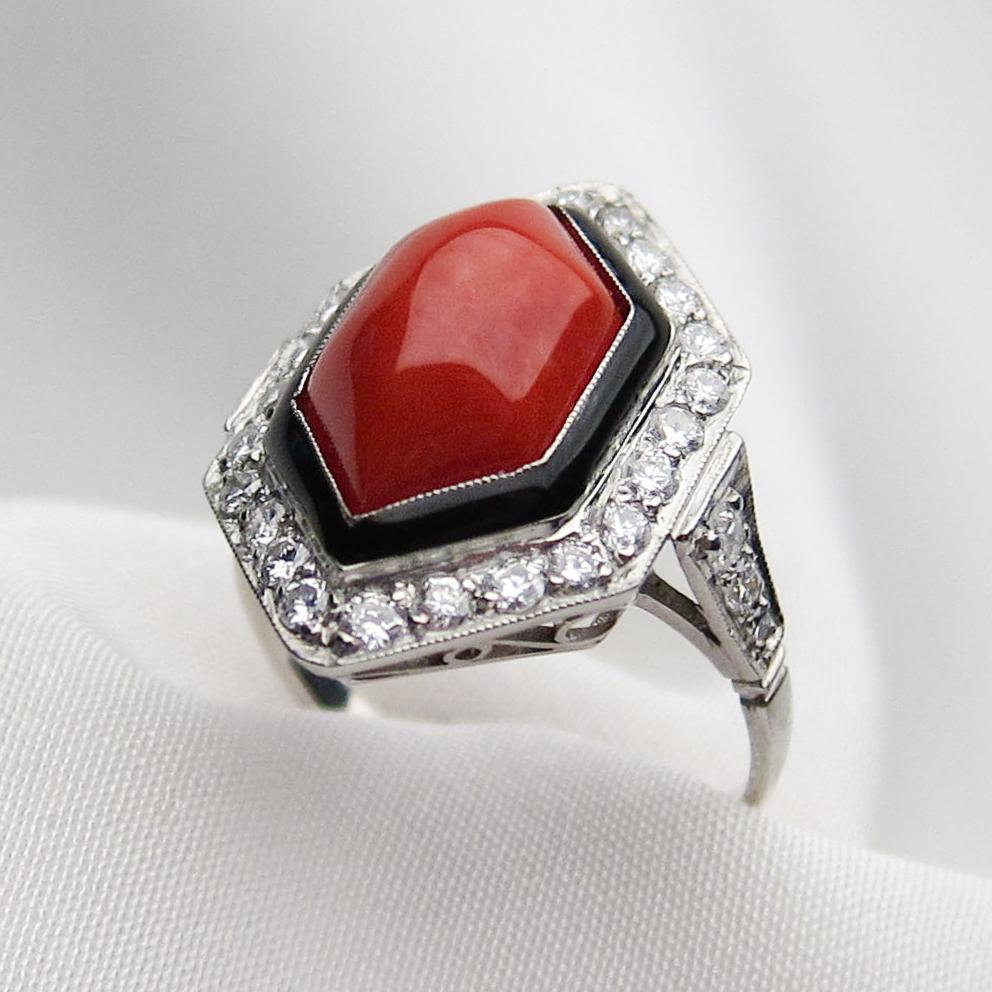 This fantastic  ring features a lovely hexagonal natural orange-red coral cabochon weighing 3.70 carats, accented with black enamel and set in platinum. 24 bead-set round brilliant-cut diamonds emphasize the coral cabochon, while three bead-set