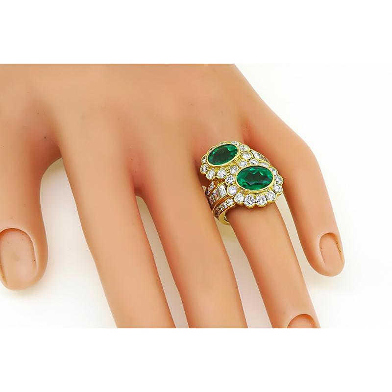 This is an elegant 18k yellow gold ring. The ring is set with 2 lovely oval cut emeralds that weigh approximately 3.70ct. The emeralds are accentuated by sparkling round and emerald cut diamonds that weigh approximately 3.41ct. The color of the