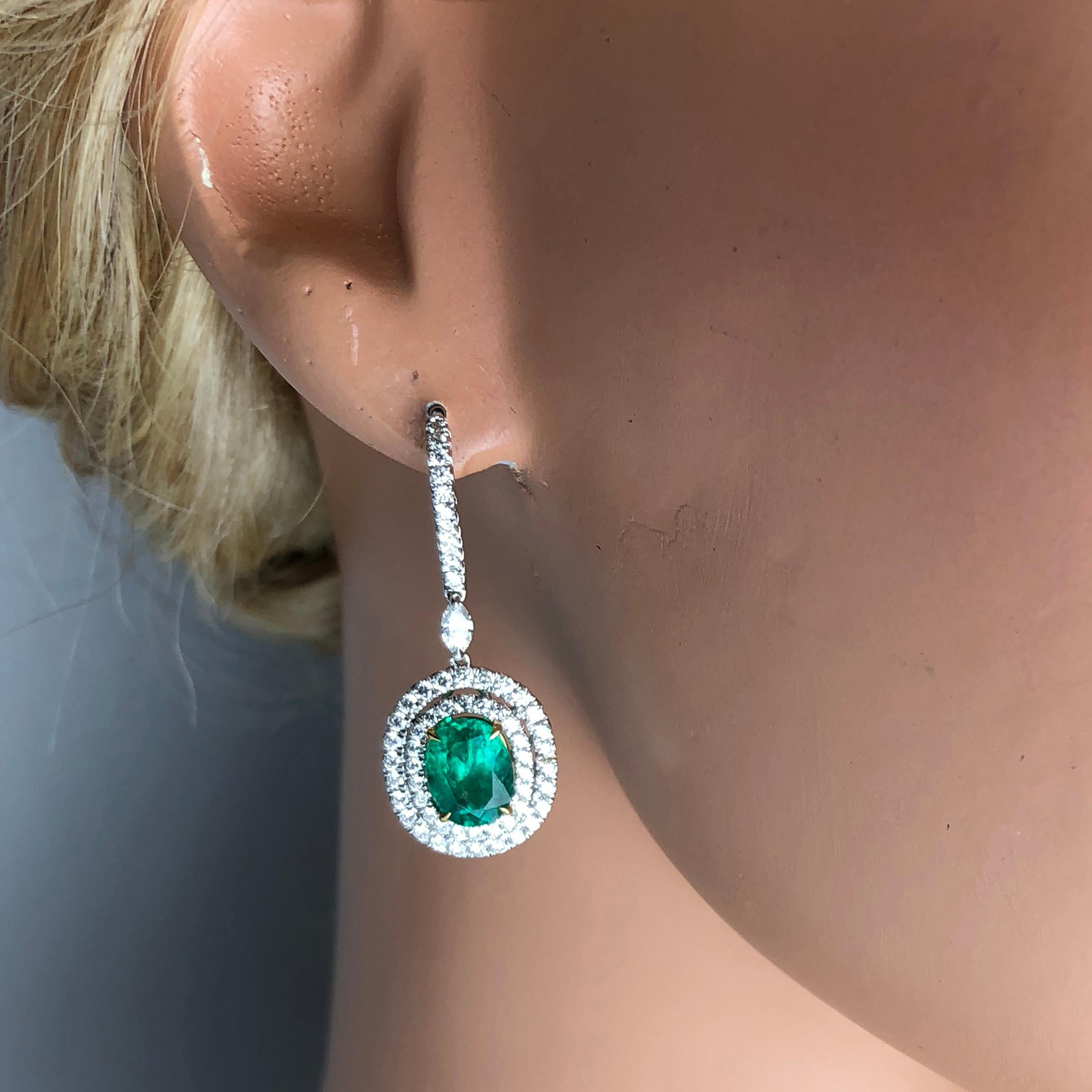 (DiamondTown) These beautiful drop dangle earrings feature 3.73 carats oval cut fine emerald, surrounded by double halos of round white diamonds. A single marquise cut diamond links the body of the earring to a lever-back hook, also featuring round
