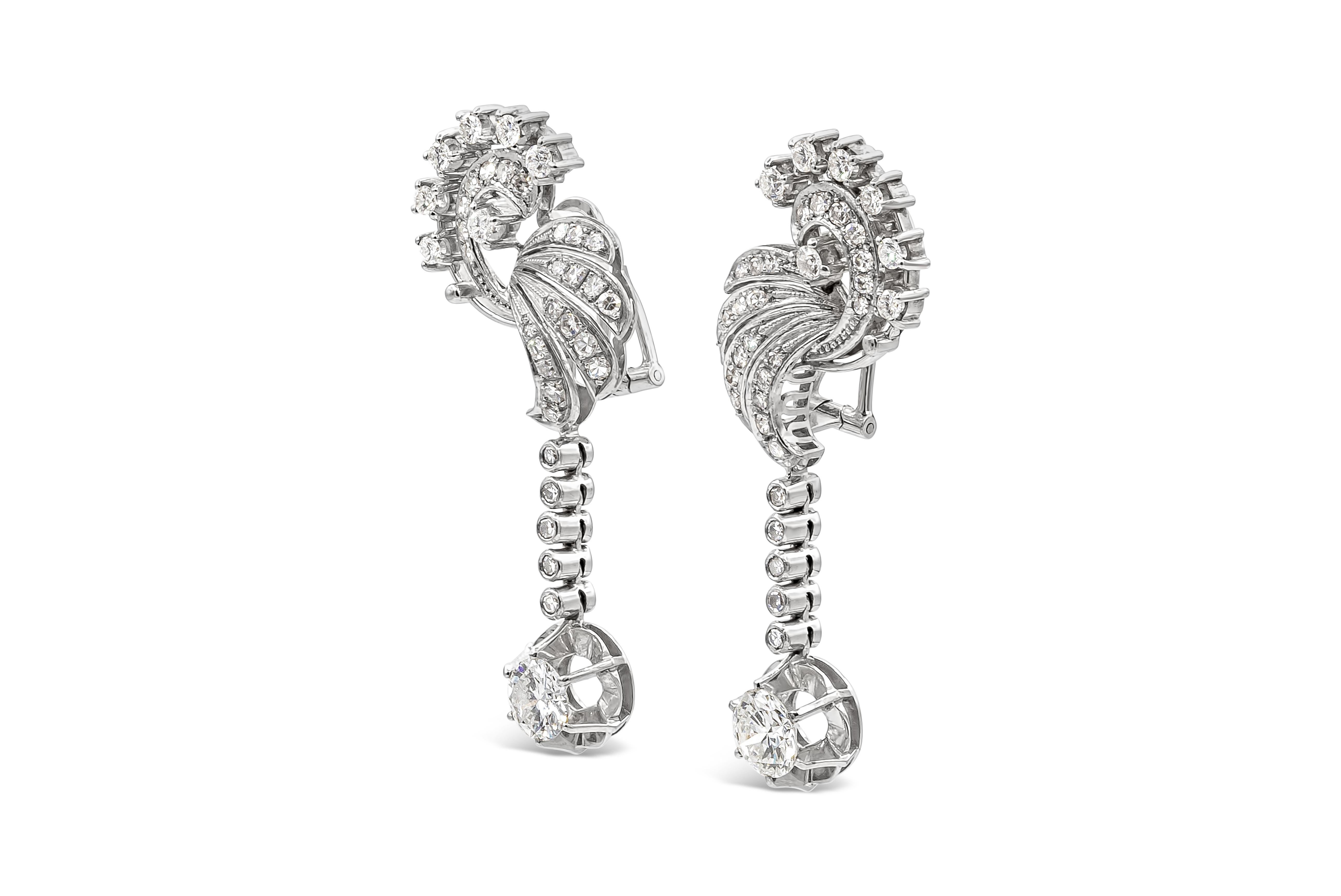 A vintage pair of dangling earrings showcasing two brilliant round diamond weighing 2.25 carats elegantly suspends in a line of bezel set round diamonds and hanging from a intricate filigree design work embellished with round melee diamonds.