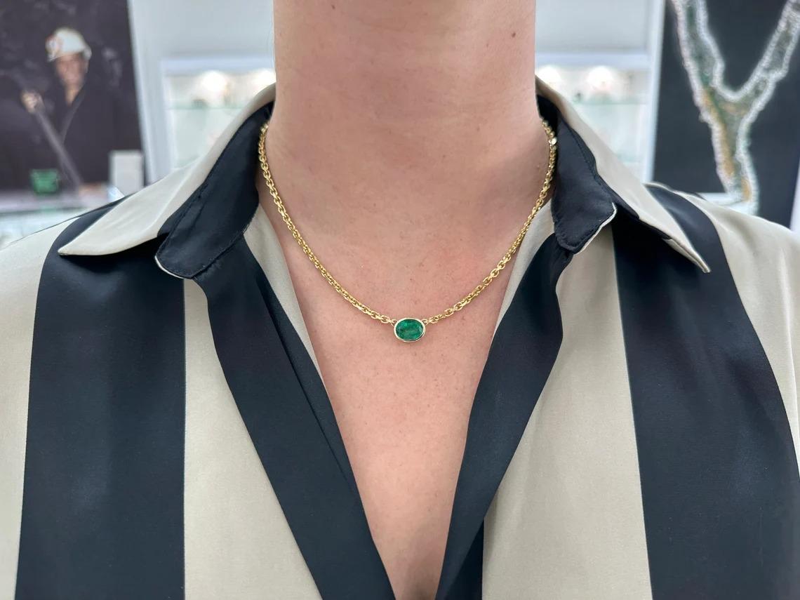 This exquisite piece of jewelry features a natural oval cut emerald from Zambia, boasting a rich dark green color that is sure to catch the eye. The emerald is securely bezel set and suspended from a 3.0 mm gold anchor chain crafted in 14k solid