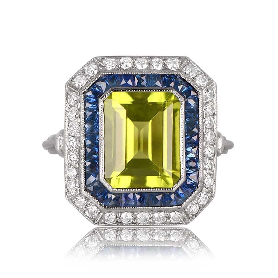 This captivating ring features a 3.77-carat peridot center stone with a rich, deep-green saturation. It is elegantly encased by two halos, one adorned with sapphires and the other with diamonds. The entire piece is set in a meticulously handcrafted