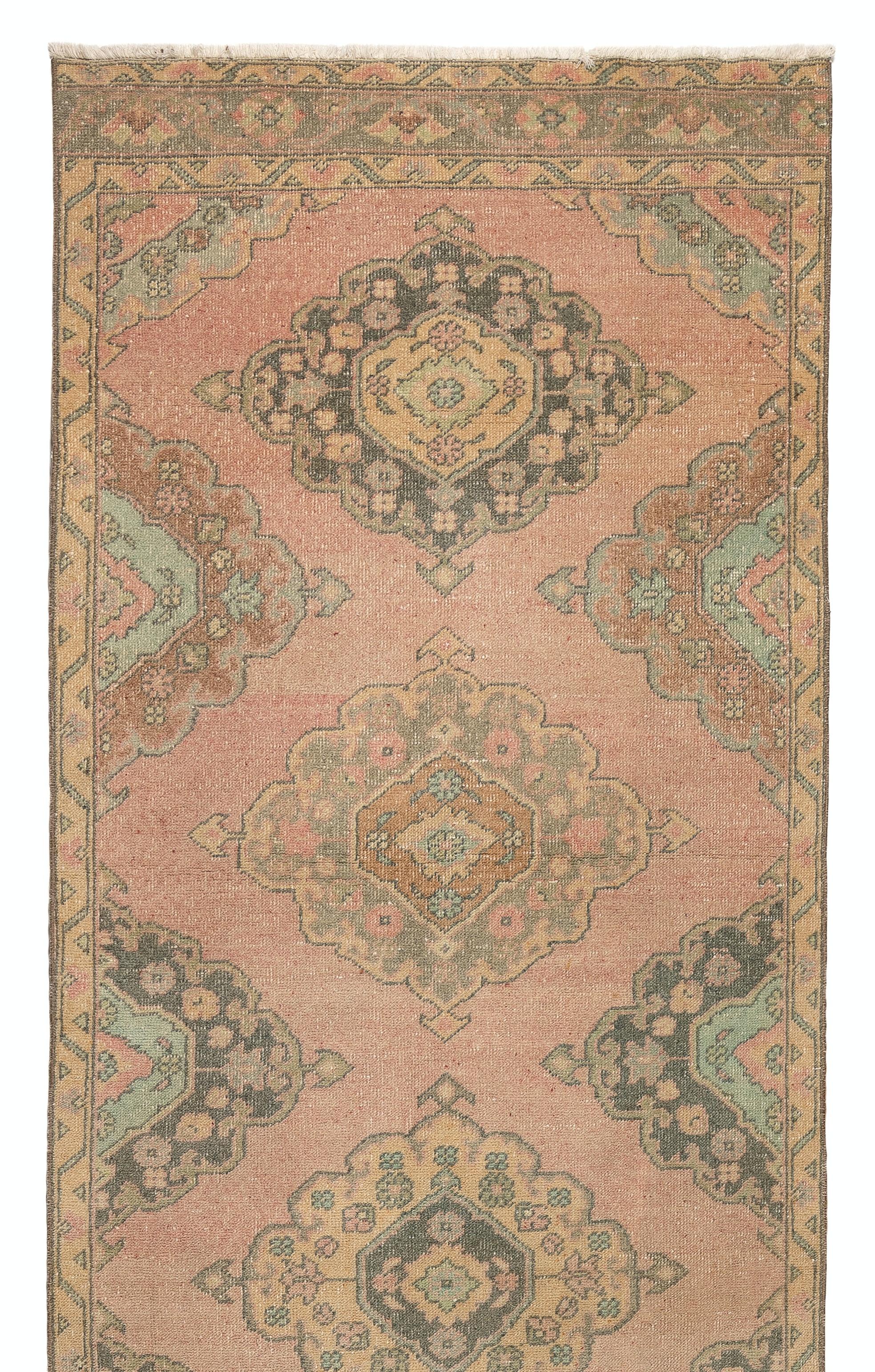 A vintage runner rug from Turkey. It is made of medium wool pile on wool foundation and features a design of multiple and half medallions running across the length of the rug in faded coral, light blue, gray and rust colors. Measures: 3.7 x 11.2
