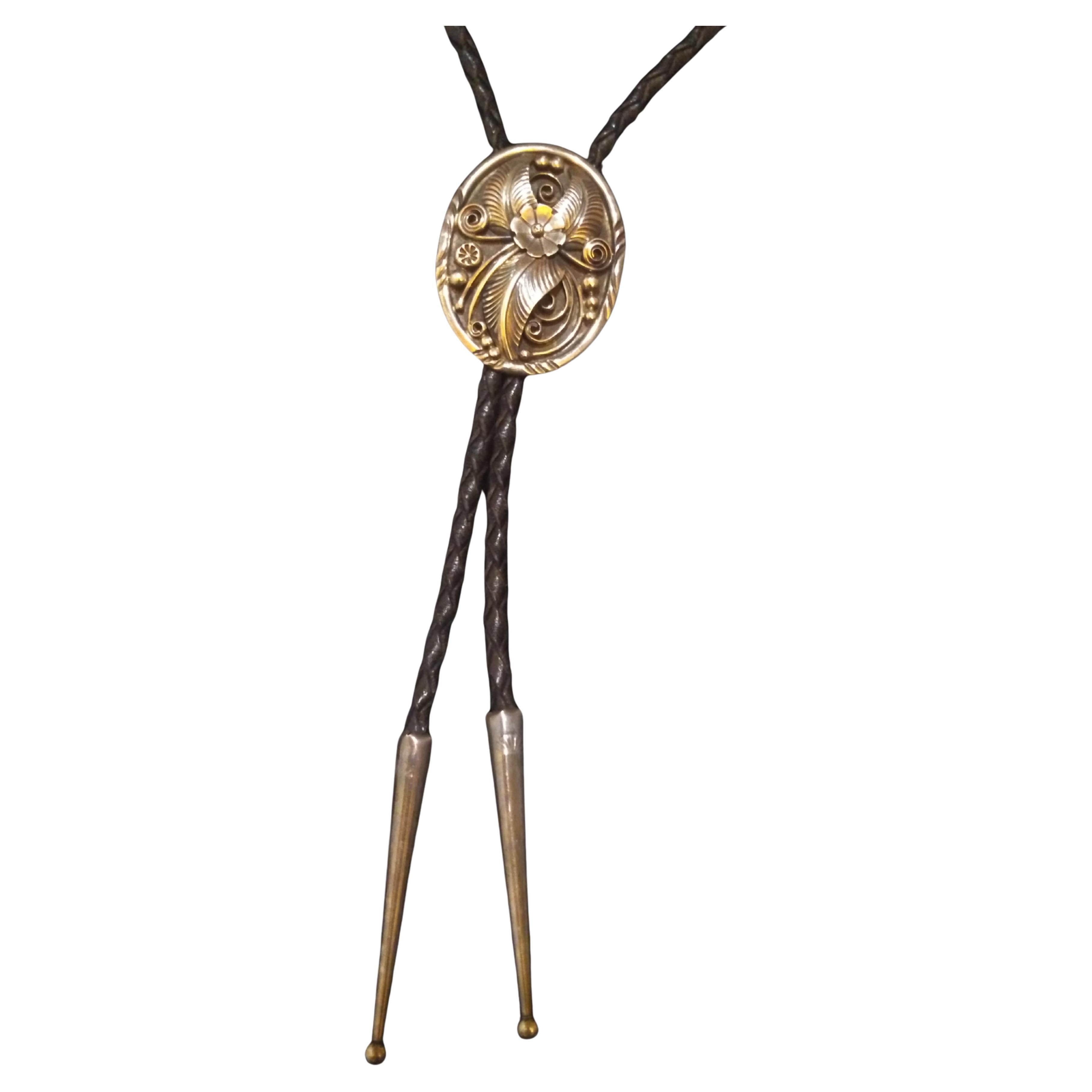 This is a beautiful bolo tie. It's made of braided leather with a sterling silver medallion that has an applied wire design. The medallion features a flower surrounded by leaves. The wire is applied in a cloisonne type way.. The tips are crafted in