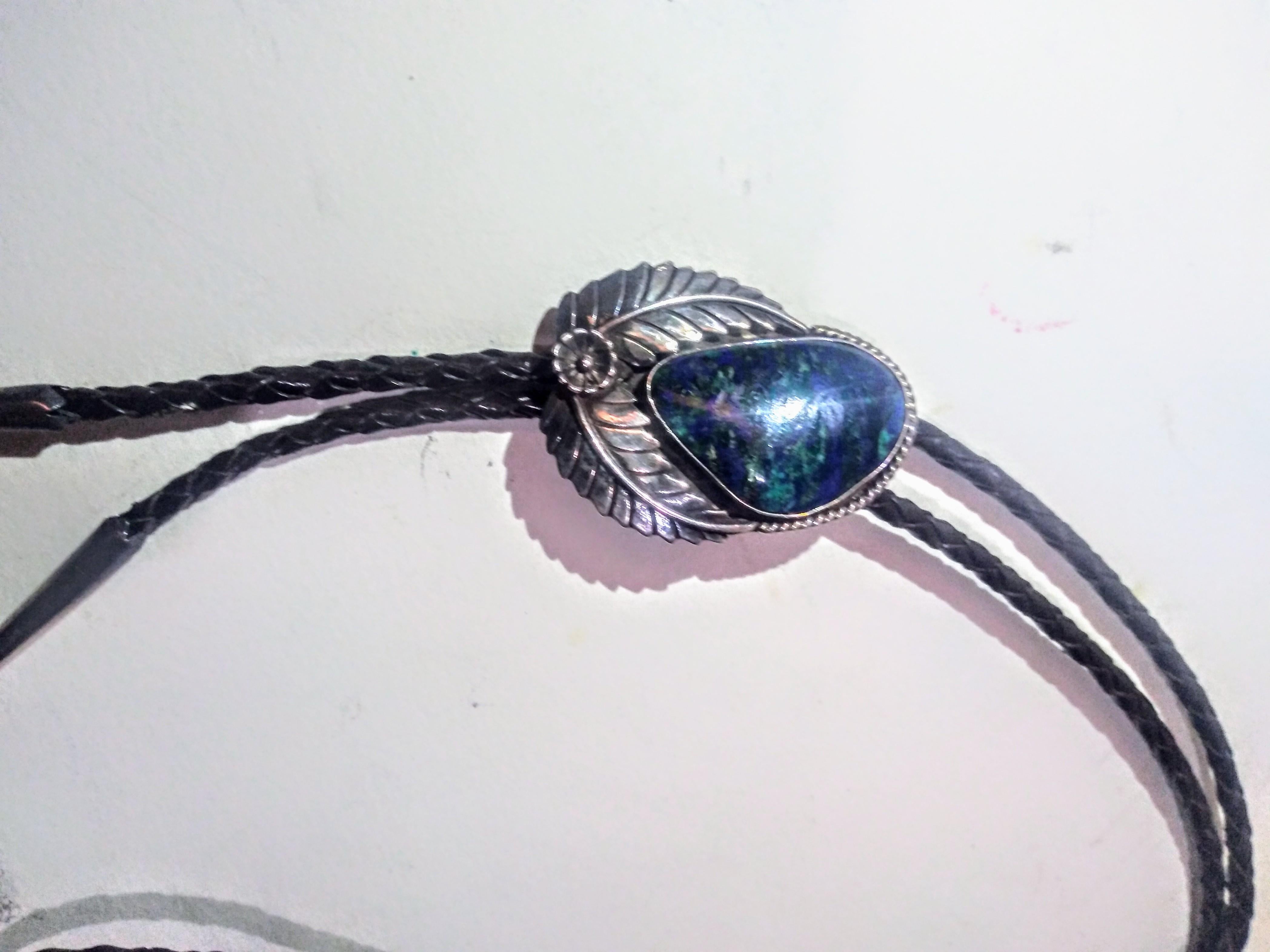 This is a beautiful bolo tie. It's made of braided leather and sterling silver with a blue opal medallion setting. design. The opal is surrounded by 2 leaves.. The tips are crafted in silver also.

The piece is signed and was made in 92'.
Signature