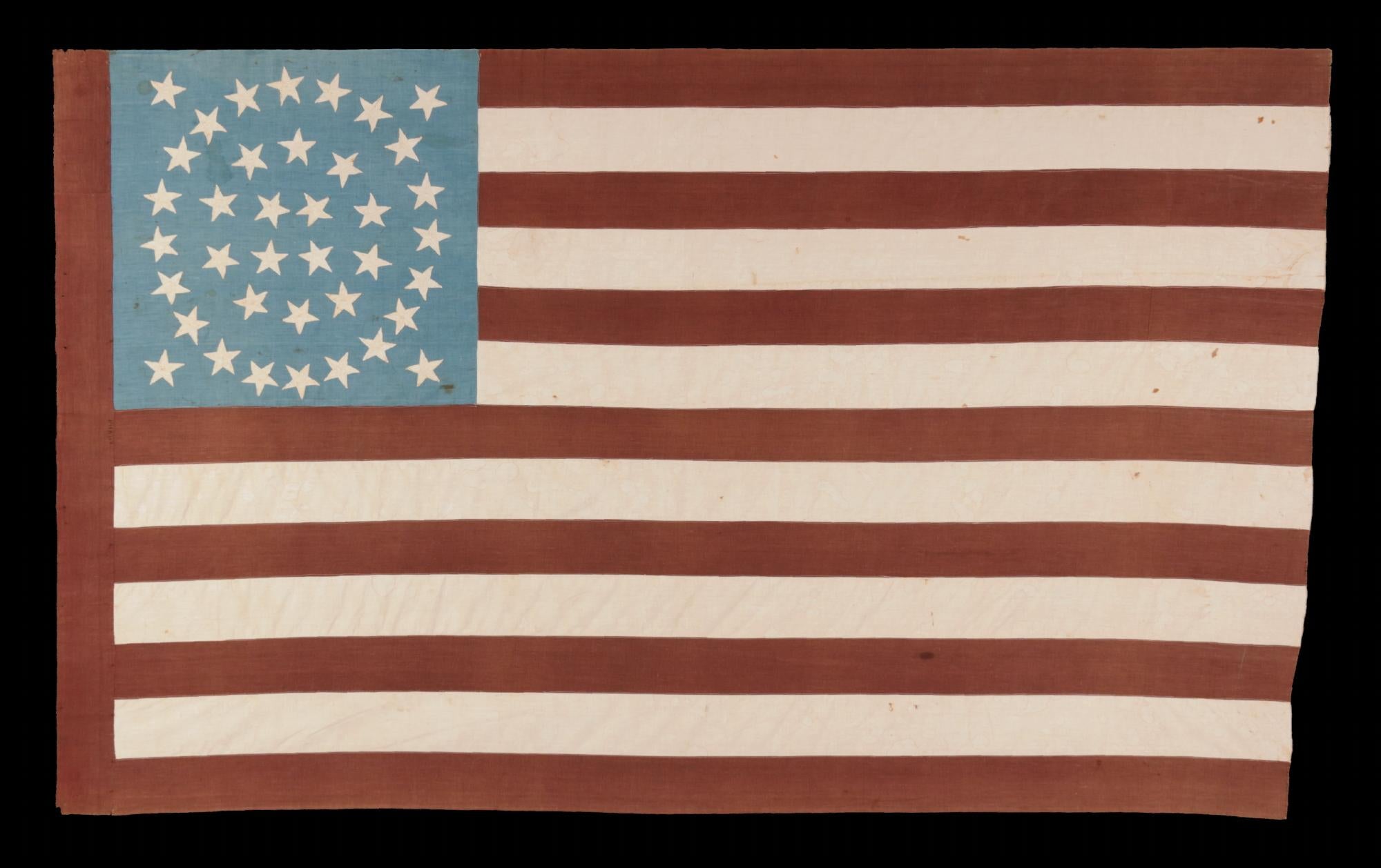 38 STAR ANTIQUE AMERICAN FLAG WITH AN EXTREMELY RARE DOUBLE-WREATH CONFIGURATION THAT FEATURES A SQUARE OF FOUR STARS BOTH INSIDE AND OUT, ON A BEAUTIFUL, CORNFLOWER BLUE CANON THAT RESTS ON THE BLOOD STRIPE, WITH A WIDE, OXBLOOD RED HOIST AND