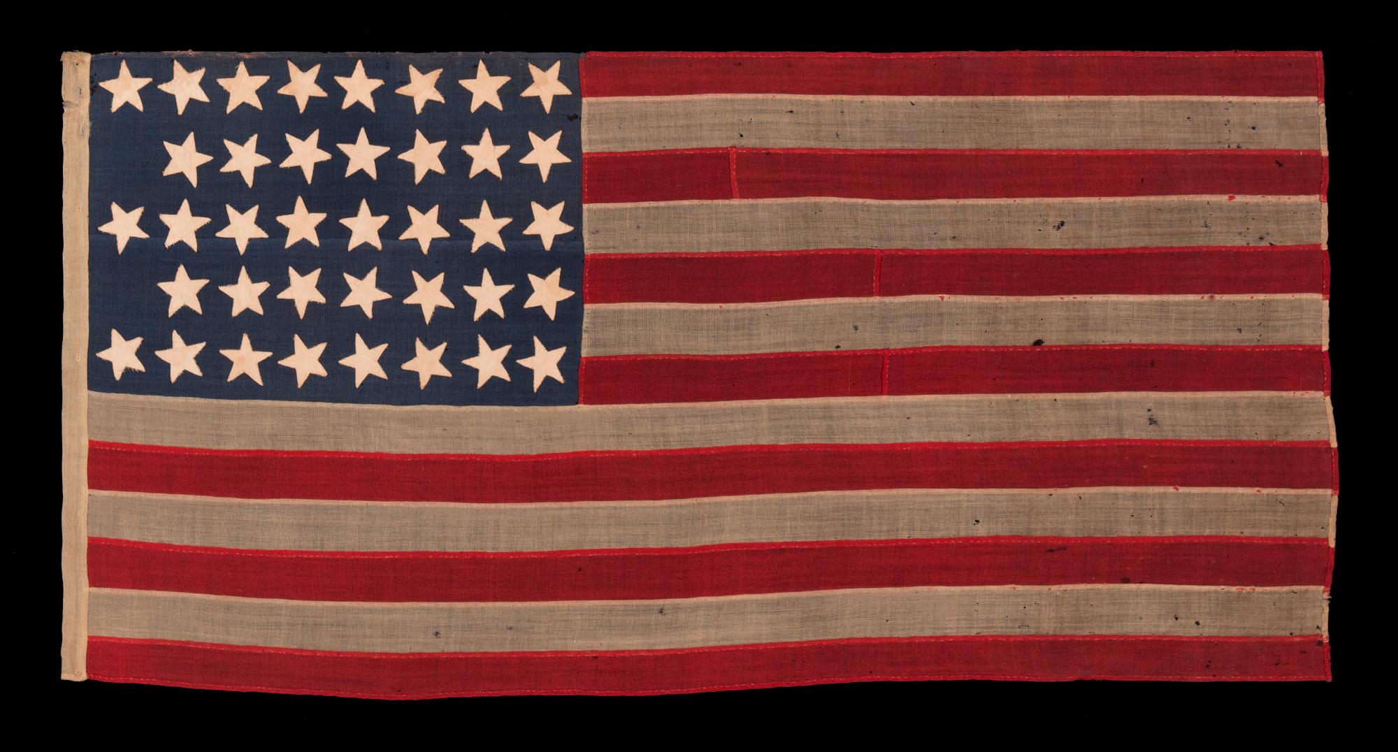 38 STAR ANTIQUE AMERICAN FLAG IN A TINY SCALE AMONG THOSE WITH PIECED-AND-SEWN CONSTRUCTION, WITH BEAUTIFUL & UNUSUAL SHADE OF BLUE AND WITH A NOTCHED CONFIGURATION OF STARS THAT LEAVES ROOM FOR WESTERN TERRITORIES THAT HAD YET TO BE ADDED; REFLECTS