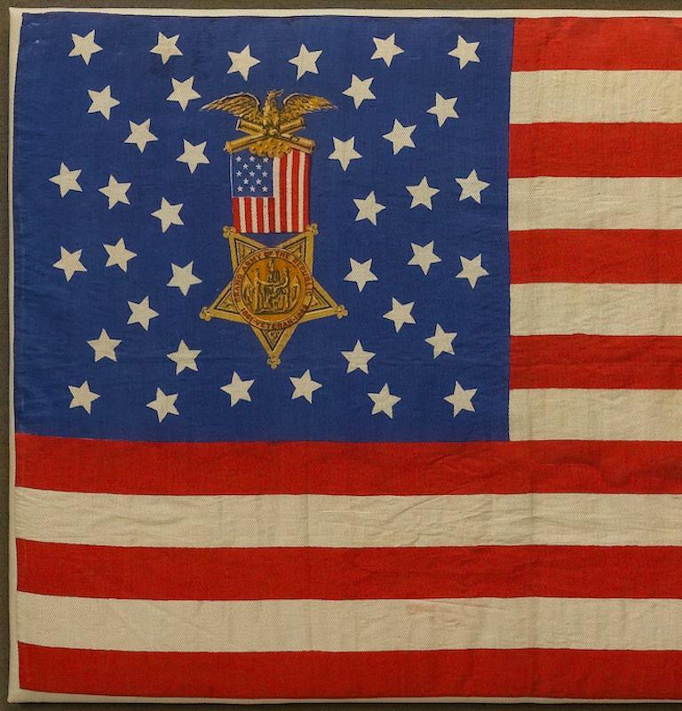 This is a beautiful and finely printed silk flag that celebrates the “G.A.R.” or Grand Army of the Republic.

The flag features the Grand Army Badge, printed on a dark navy blue canton. The Grand Army Badge is composed of an eagle on crossed cannons