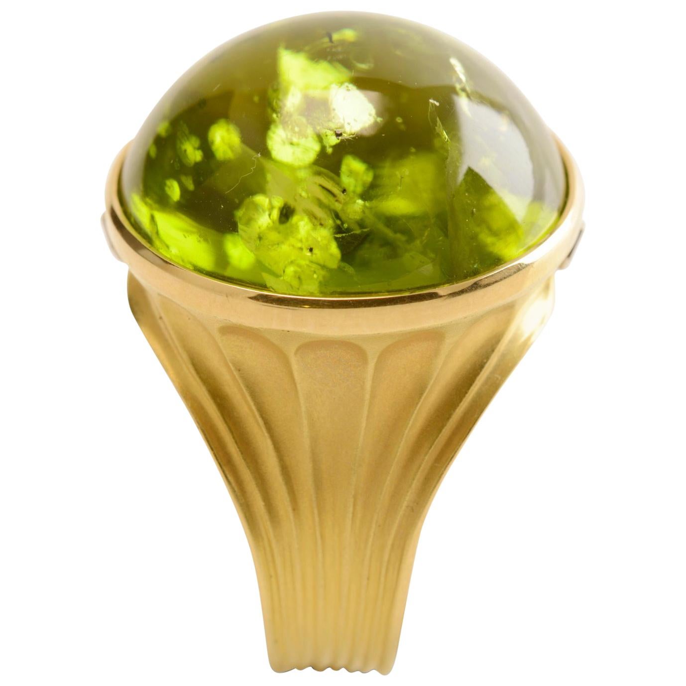 A magnificent peridot cabochon of 38.40 carats sits in an 18 karat yellow gold hand forged setting, a cocktail or dress ring that truly pushes the boundaries of what can be made in gold. The shank is gently concaved from the base and detailed with