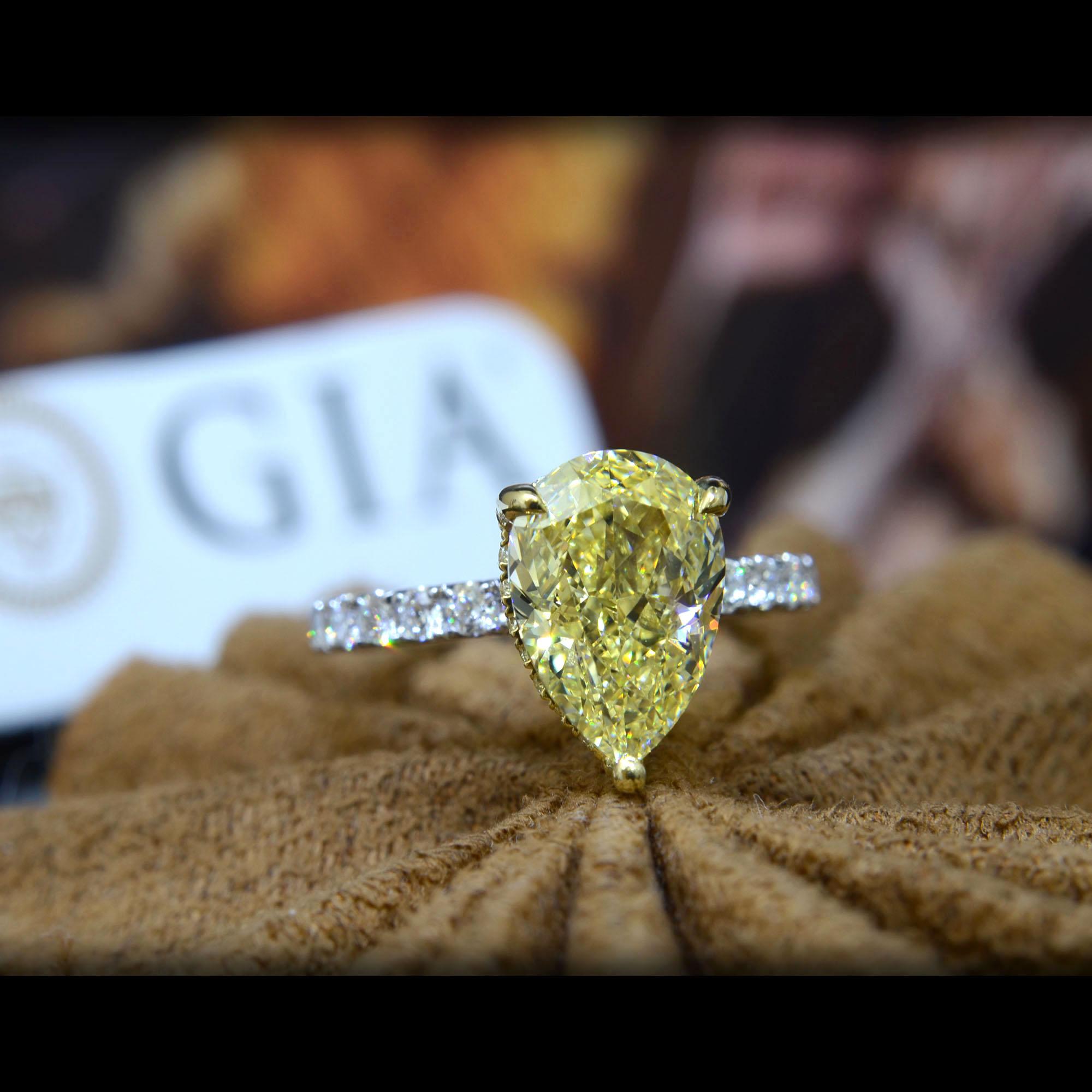This gorgeous canary diamond ring flaunts a lovely GIA certified 2.70 Ct. Pear shape diamond with natural canary Fancy Yellow color and VS2 clarity. Surrounding the center stone in hidden halo and down the shank are 0.65 ct. total weight Round cut