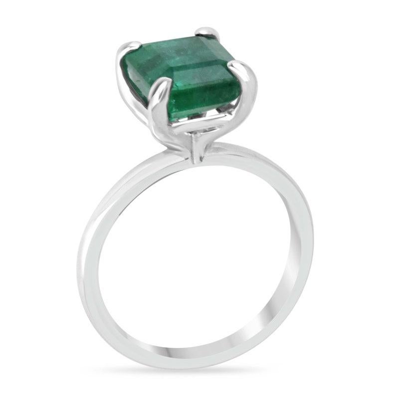 Adorn yourself with the timeless elegance of our solitaire emerald ring, featuring a 3.85 carat emerald-cut emerald set north to south. This gemstone showcases a deep green color, very good luster, and semi-transparent clarity, making it truly