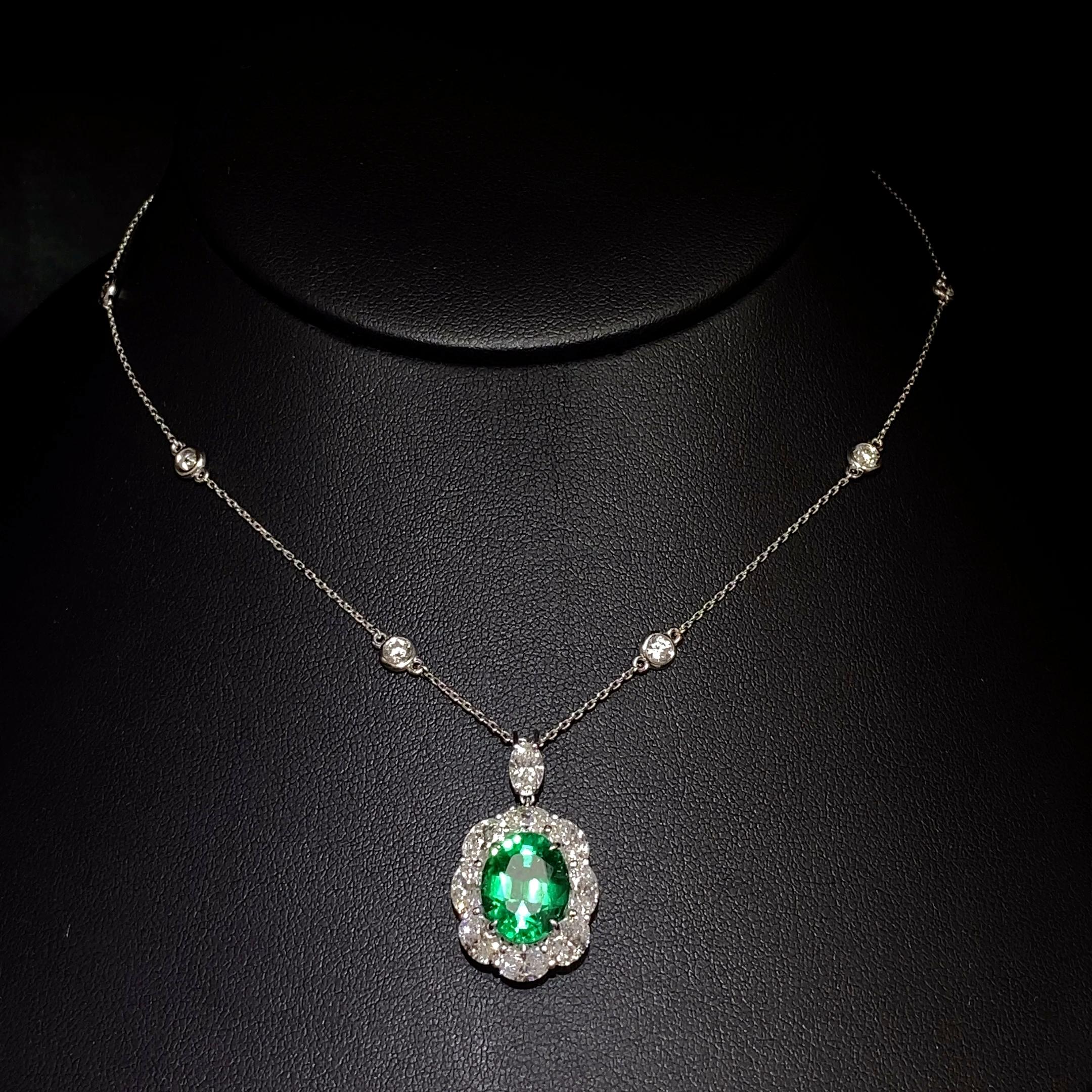 A classic pendant necklace showcasing an Oval shape, lush green emerald weighing 3.88 carats total. Surrounded by a row of oval diamonds, weighing 1.88 carats total. Suspended on a marquise shape diamond halo surmount attached to a diamond by a yard