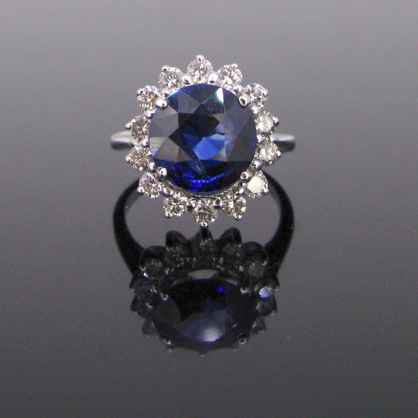 This beautiful ring is set with a 3.88ct deep blue sapphire. The sapphire is surrounded with 14 brilliant cut diamonds for a total carat weight of 0.80ct approximately. The ring is fully made in 18kt white gold. It is controlled with the ring band