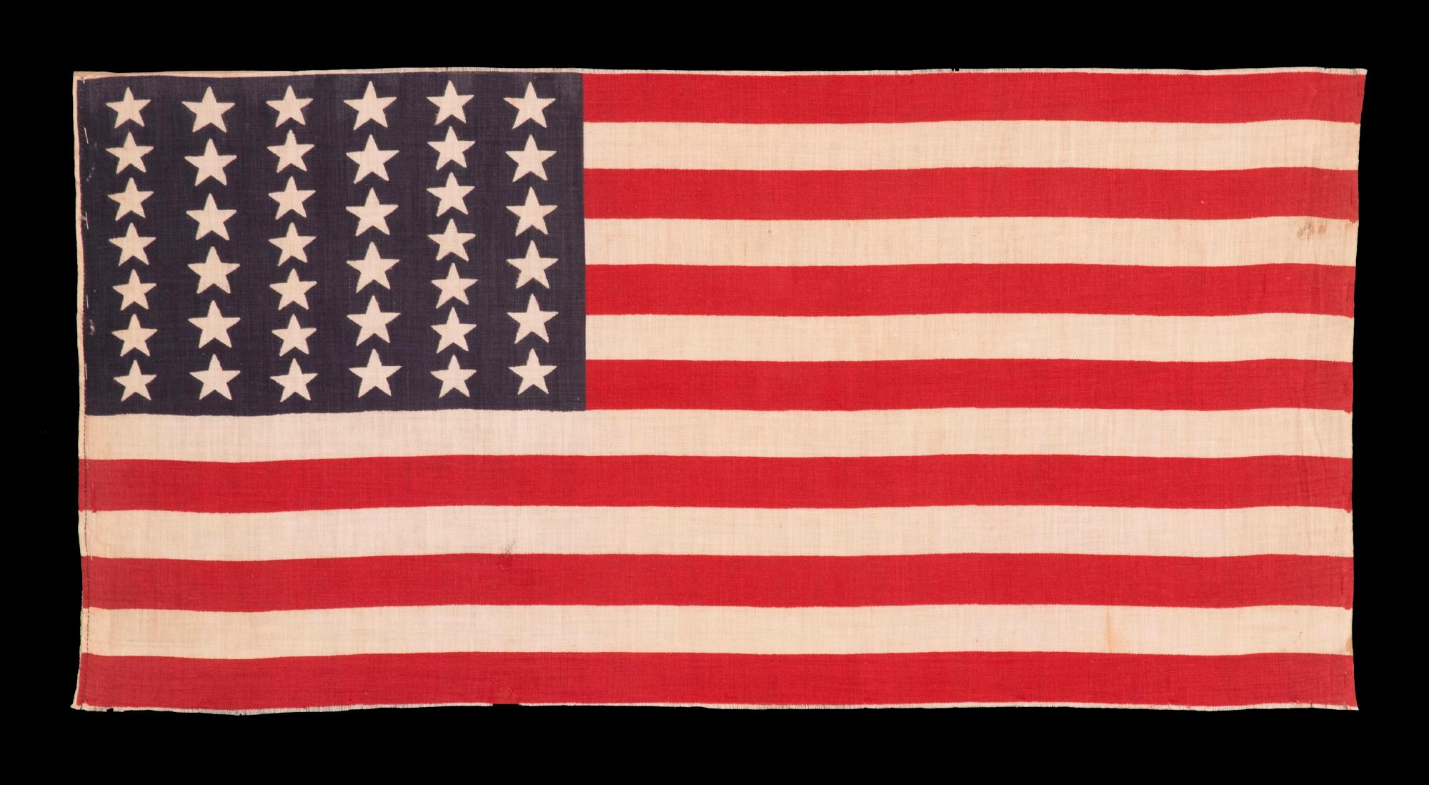 39 STARS IN TWO SIZES, ALTERNATING FROM ONE COLUMN TO THE NEXT, ON AN ANTIQUE AMERICAN PARADE FLAG WITH AN UNUSUALLY ELONGATED PROFILE, DATING TO THE 1876 CENTENNIAL, NEVER AN OFFICIAL STAR COUNT, REFLECTS THE ANTICIPATED ARRIVAL OF COLORADO AND THE