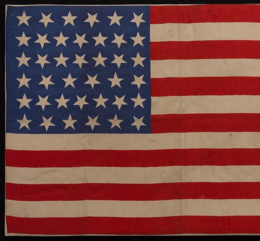 This is a 39-star unofficial American flag, printed on silk. The flag dates to 1889 showcasing a “whimsical” star pattern in the canton. An official flag with only 39 stars was never approved by Congress. Printmakers often gambled on how many states
