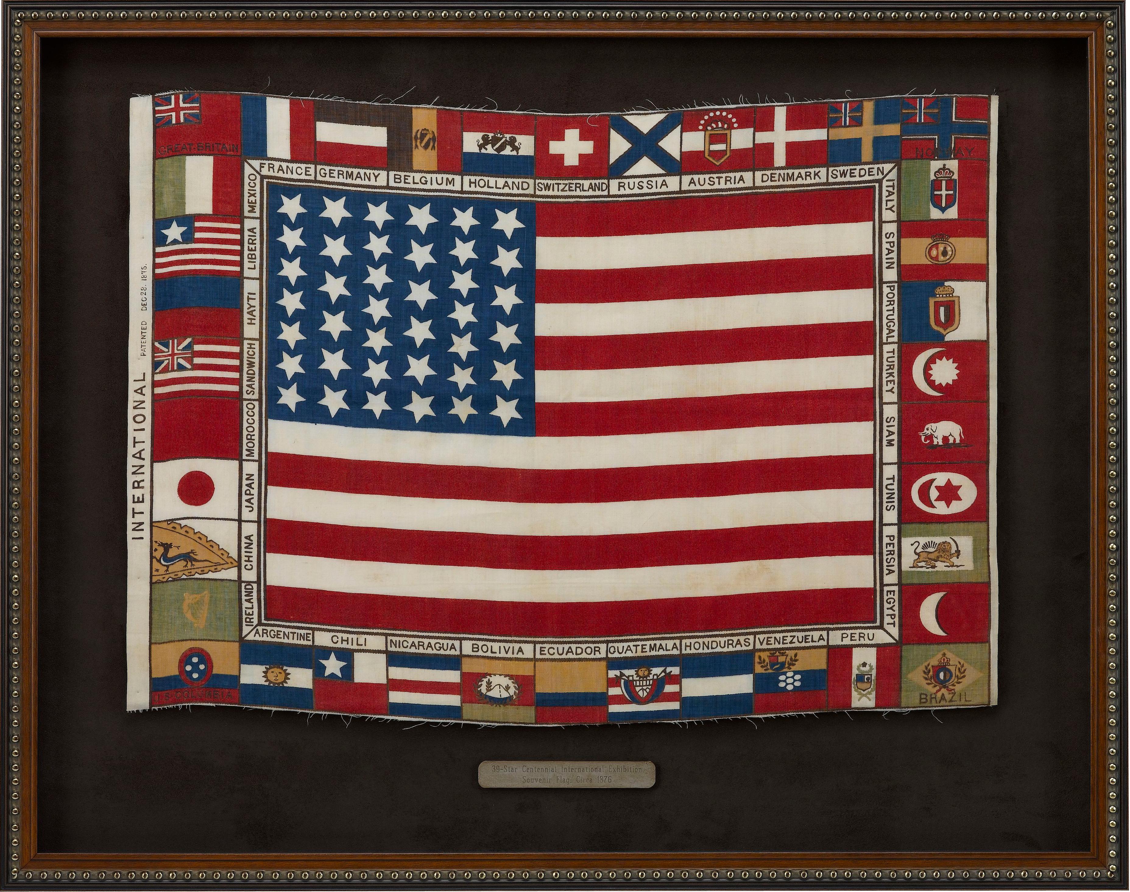 This is a patriotic Centennial Exhibition textile featuring a 39-star American flag at center, surrounded by a border of 38 other flags of the world. The hoist is printed with “INTERNATIONAL Patented Dec 28. 1875.” 

This souvenir flag was printed