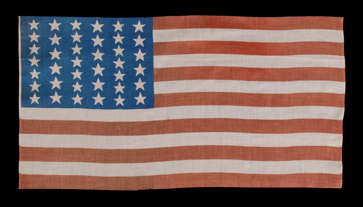 39 STARS IN TWO SIZES, ALTERNATING FROM ONE COLUMN TO THE NEXT, ON AN ANTIQUE AMERICAN PARADE FLAG WITH AN UNUSUALLY ELONGATED PROFILE, DATING TO THE 1876 CENTENNIAL, NEVER AN OFFICIAL STAR COUNT, REFLECTS THE ANTICIPATED ARRIVAL OF COLORADO AND THE