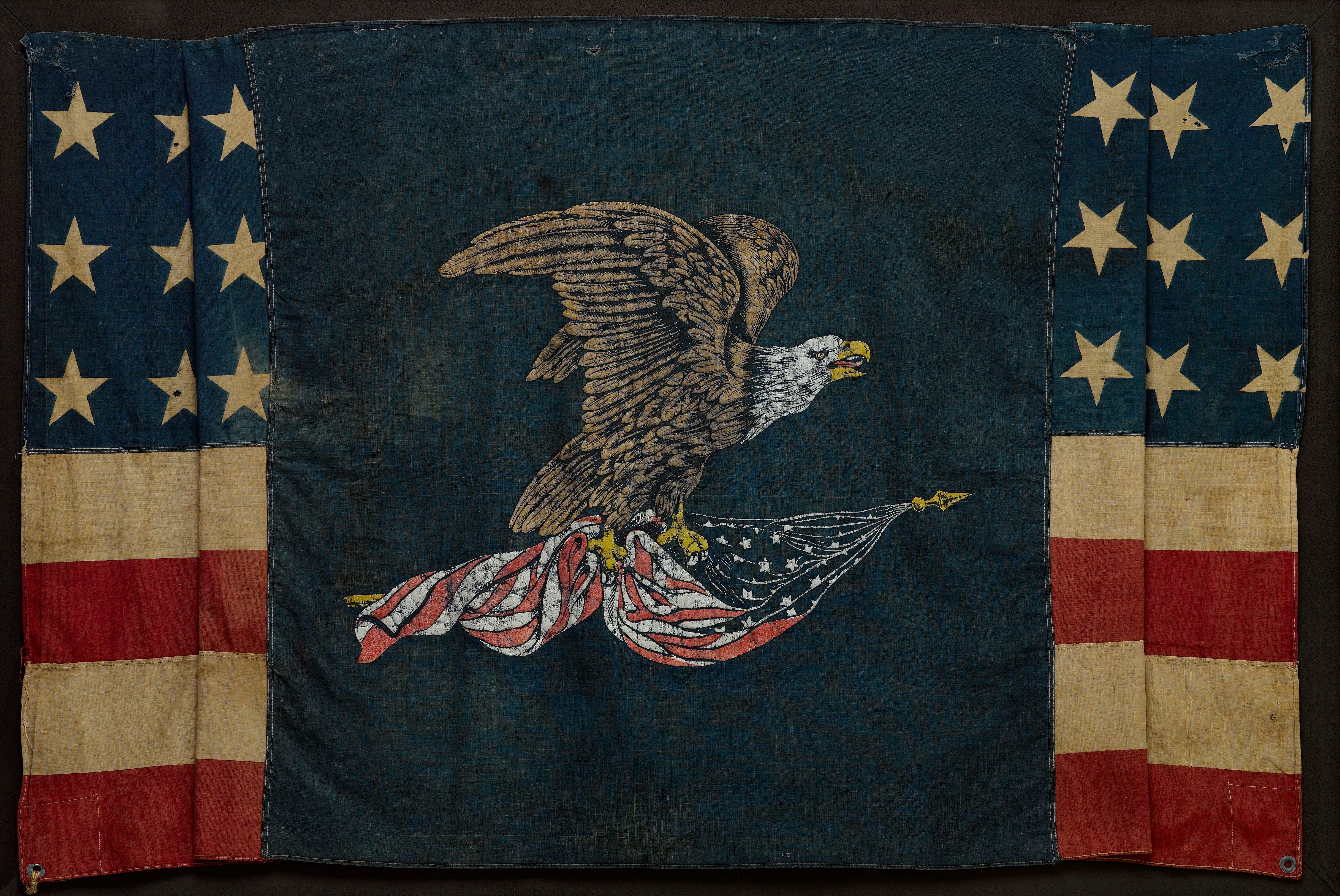 Presented is a stunning, 39-star patriotic banner commemorating North Dakota statehood. A large and dramatic polychrome eagle is printed on the center of a dark blue cotton field. The bald eagle is depicted mid-flight and clutches an American flag