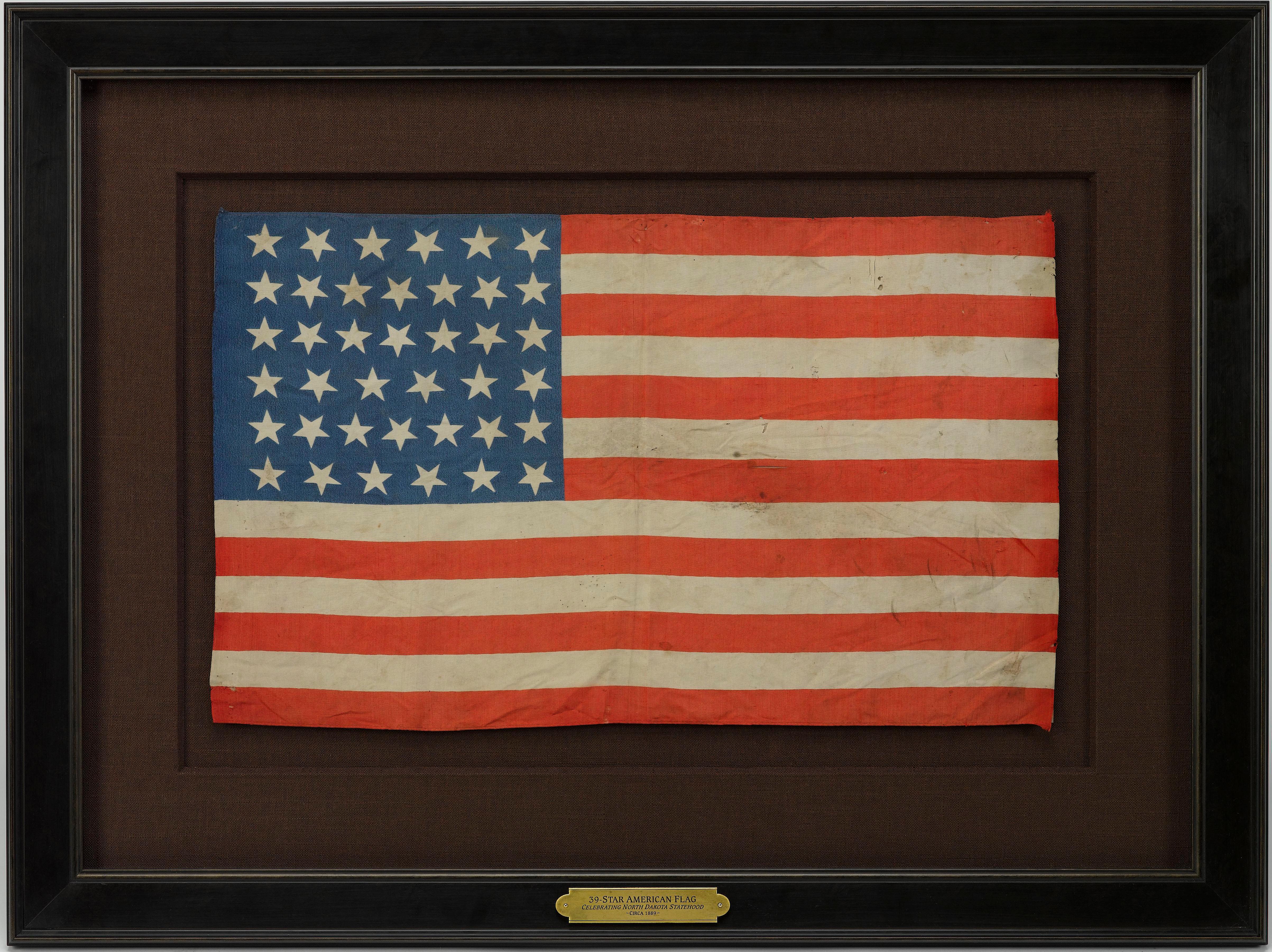 This is a 39-star unofficial American flag, printed on silk. The flag dates between 1877 and 1889, showcasing a whimsical star pattern in the canton. The flag's canton boasts a 6/7/7/6/7/6 row pattern of white stars printed on a dark blue ground.