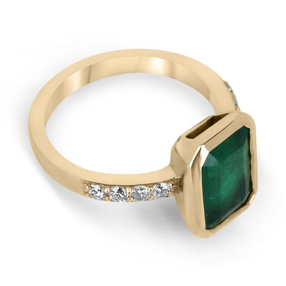 A glowing fine quality Zambian emerald bezel and diamond accent ring. This spectacular piece features an elongated emerald cut emerald; the gemstone showcases a rich dark green color that is vivacious and lustrous. Securely bezel set for the