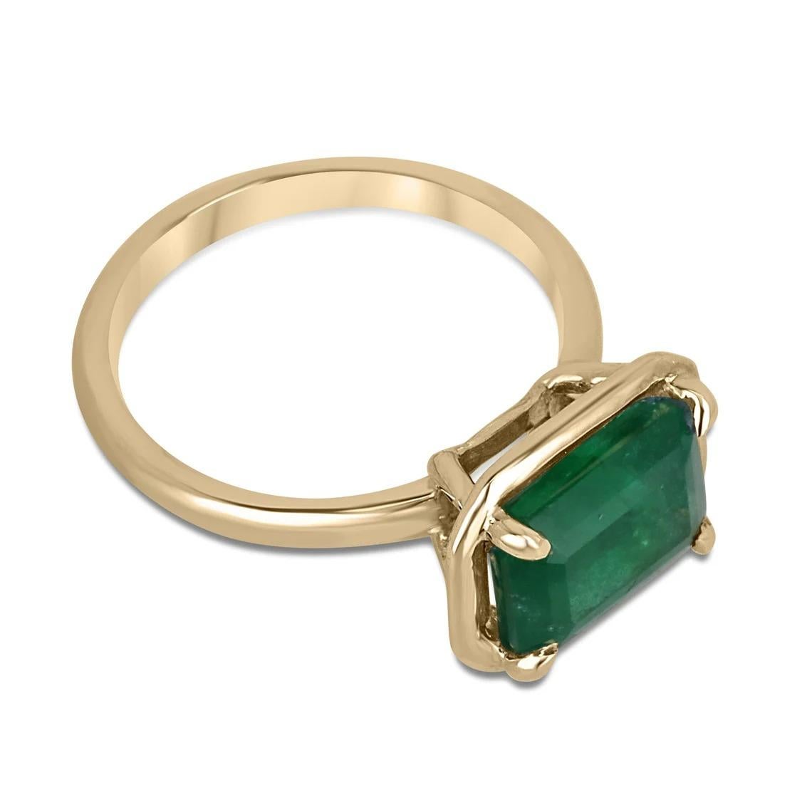 This stunning solitaire ring features a breathtaking 3.92-carat natural emerald cut emerald, set in a unique east-to-west orientation and held securely in place by a four-claw prong setting with a half-bezel design. The gemstone boasts a deep, rich