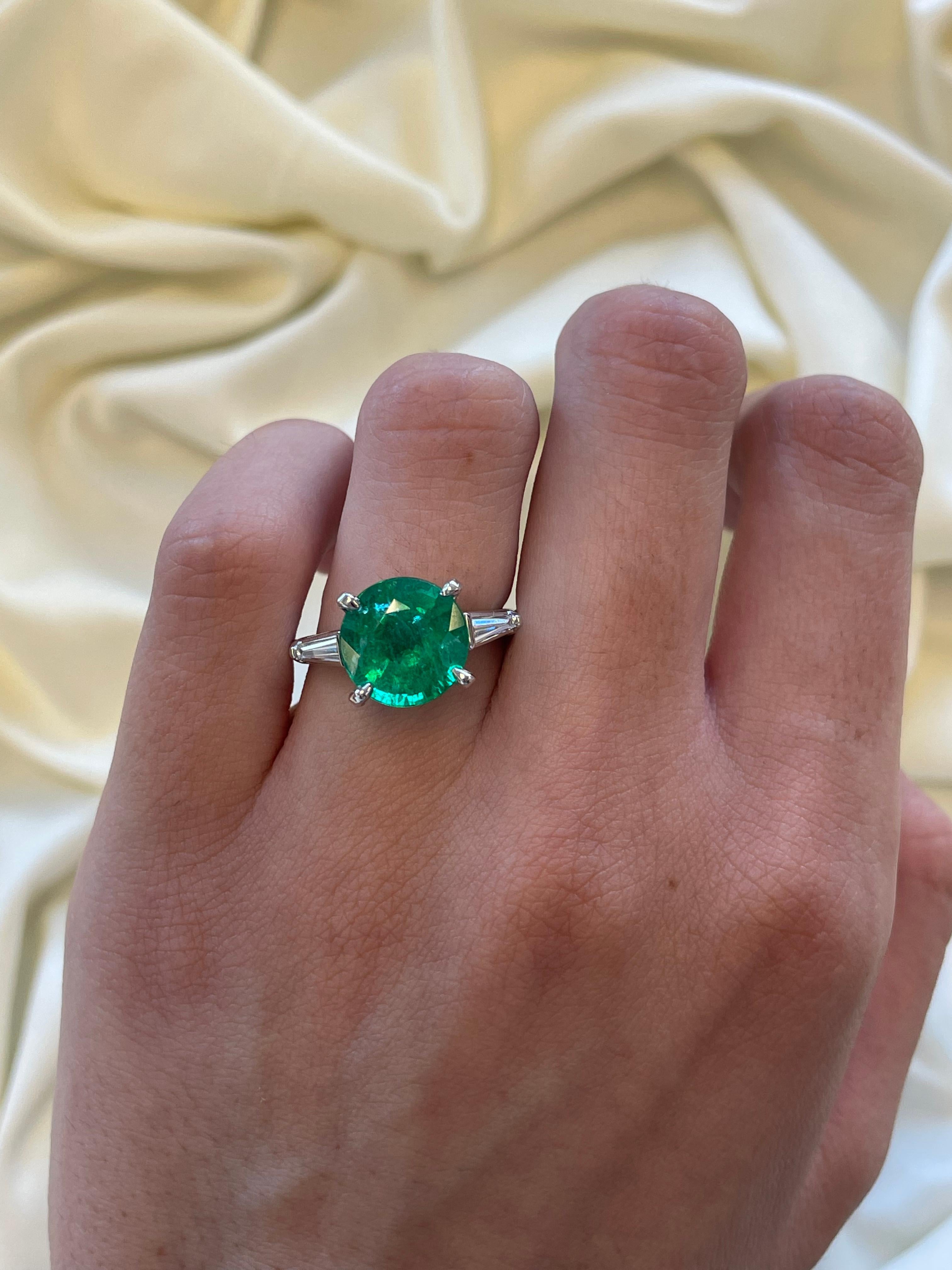 Stunning modern emerald and tapered baguette diamond three-stone ring. 
3.92 carat round cut emerald, apx F2. Complimented by 2 tapered baguette cut diamonds, 0.35 carats. Approximately G/H color and VS clarity. Platinum, 7.08 gram, current ring