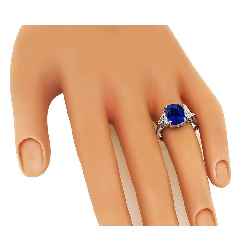 This is a magnificent platinum engagement ring. The ring is centered with a lovely cushion cut sapphire that weighs approximately 3.98ct. The sapphire is accentuated by sparkling trilliant cut diamonds that weigh approximately 0.80ct. The color of
