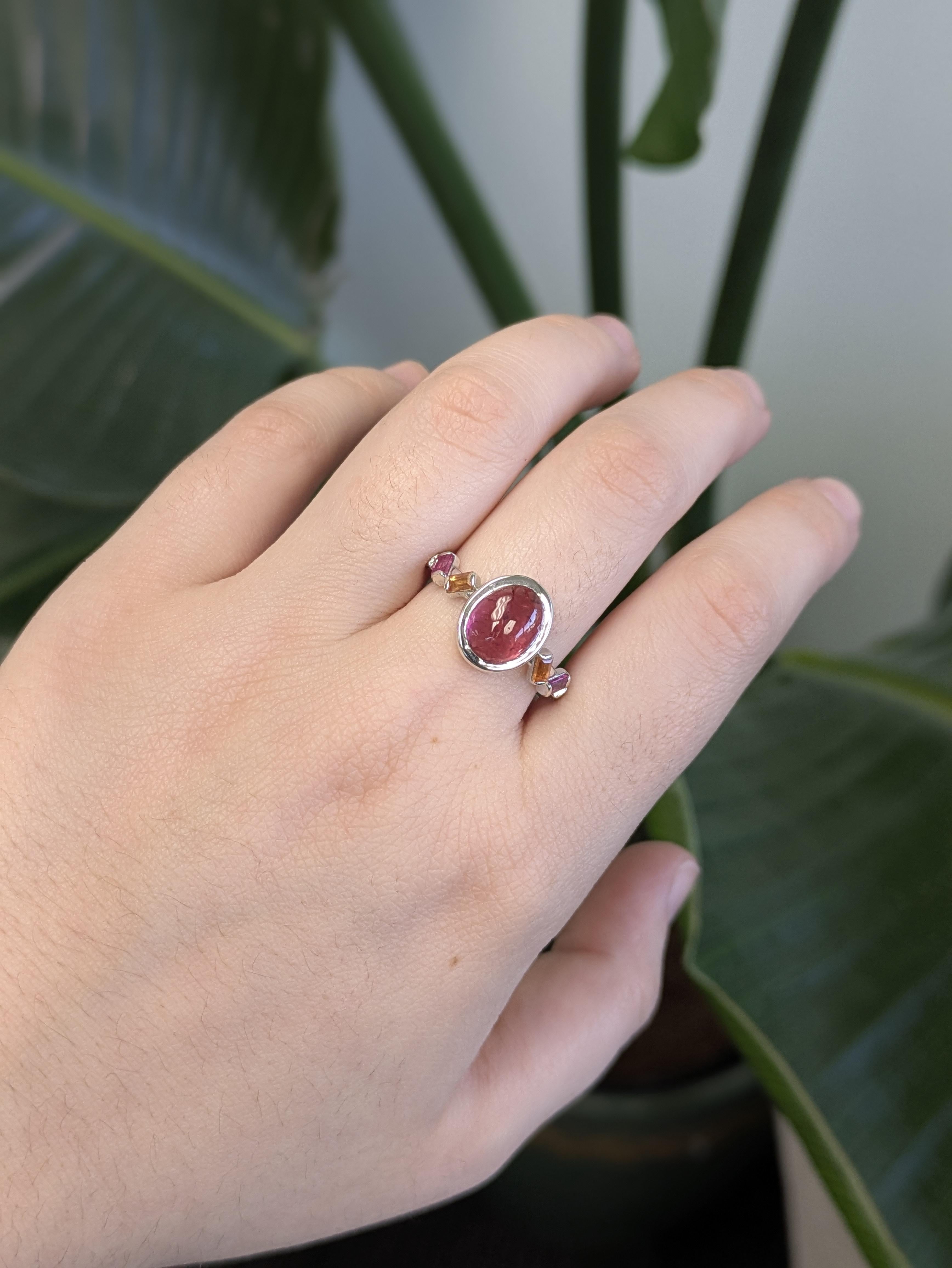 Dieser exquisite Ring zeigt einen ovalen Rubin in der Mitte, der von schimmernden Saphiren akzentuiert wird und in massivem 14-karätigem Weißgold gefasst ist. Die perfekte Mischung aus feuriger Eleganz und kühler Raffinesse ist ein zeitloser