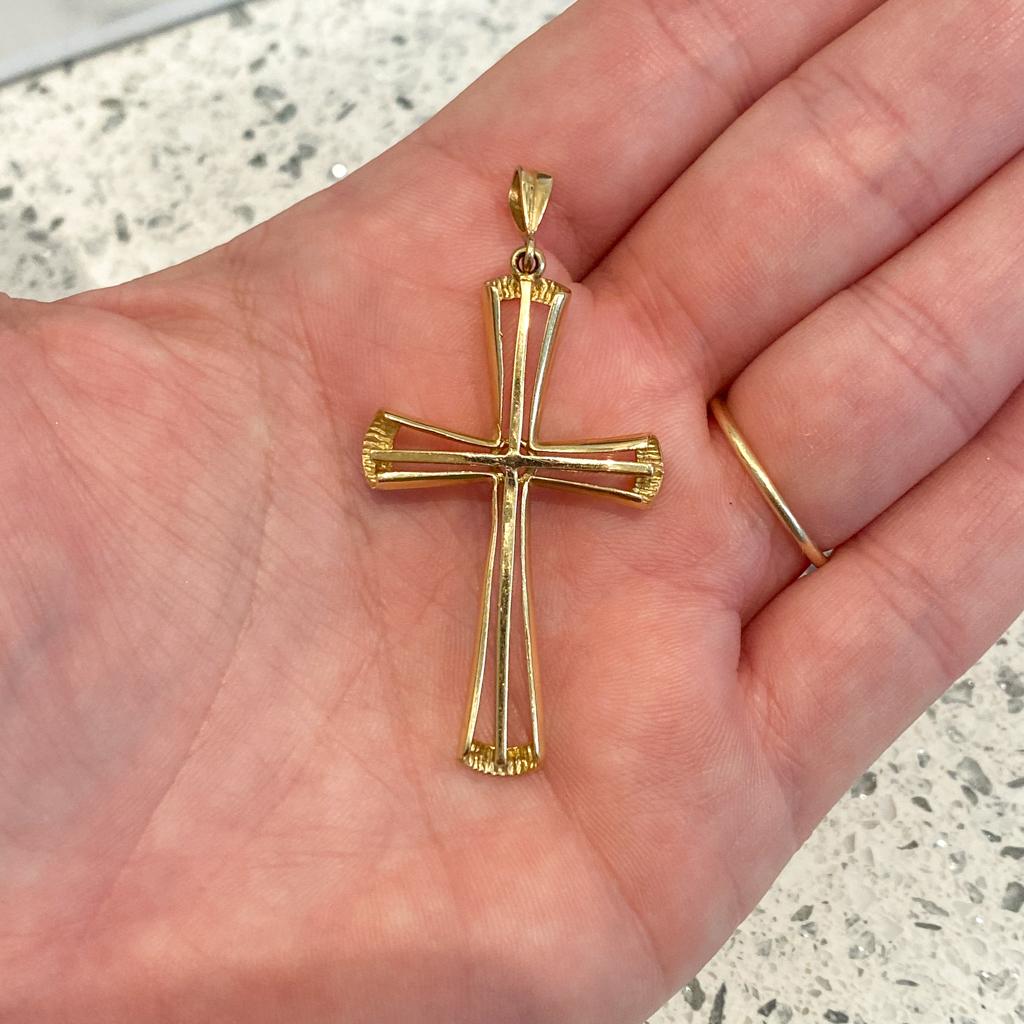 This elegant cross pendant is made in sturdy 14 karat gold with a bright polish finish. The slim cross centered in the pendant is accented by the curving frame that broadens at the ends to form a  larger cross. The inside of the ends are textured to