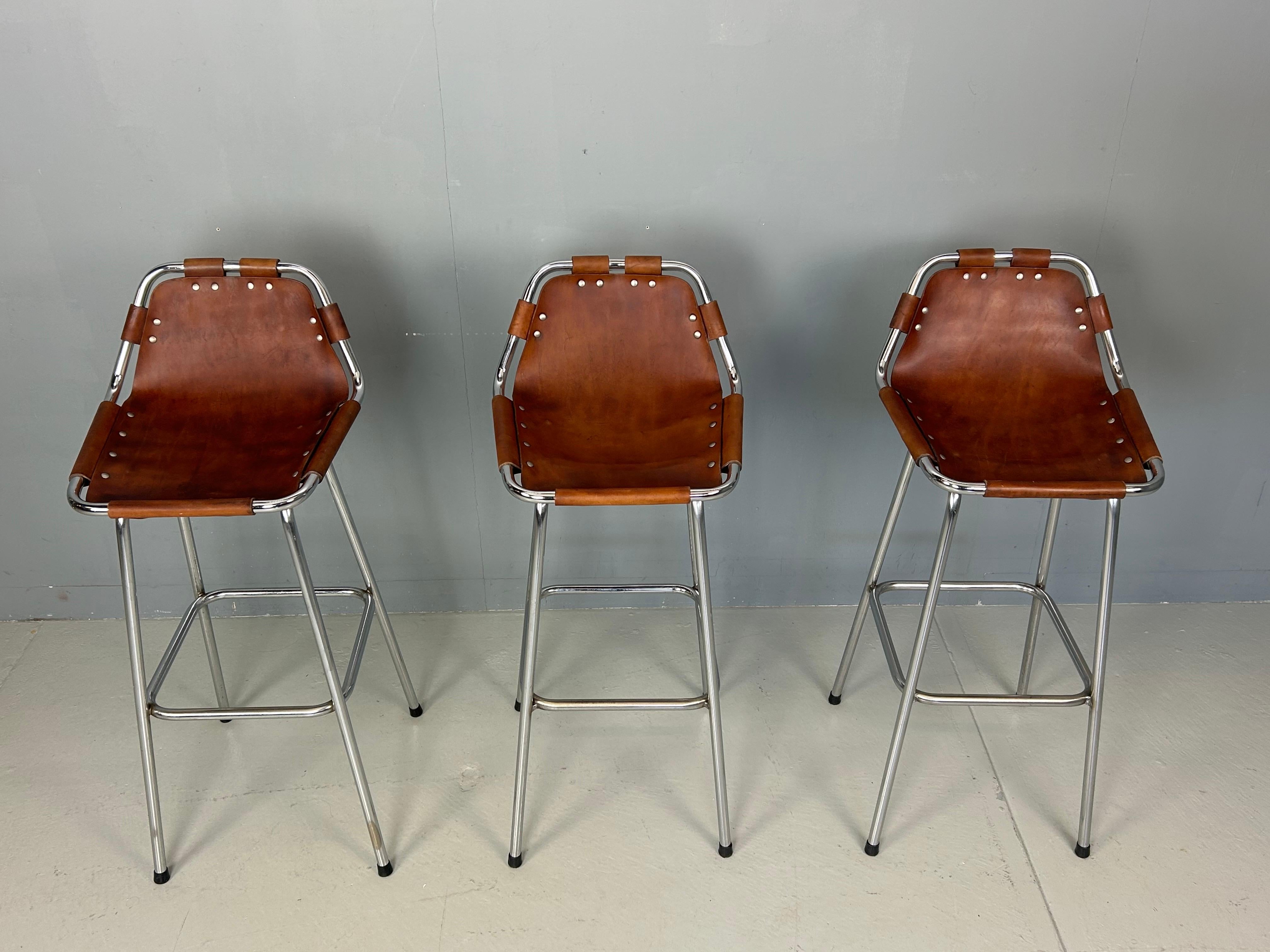 Bar stools designed by Charlotte Perriand for the renowned Les Arcs Ski Resort in France during the 1960s. Each stool features a chrome-plated tubular metal frame and seats crafted from rich cognac leather, which has aged beautifully over the years