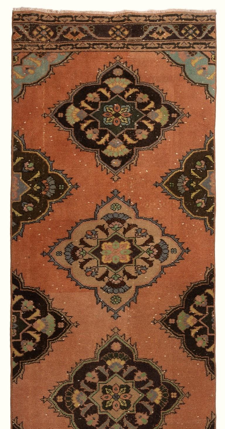 This vintage Turkish runner rug was hand-knotted in the 1970s. It features multiple full and half medallions decorated with floral motifs in brown, light green, salmon pink and slate blue against a rust-colored field. It has medium wool pile on