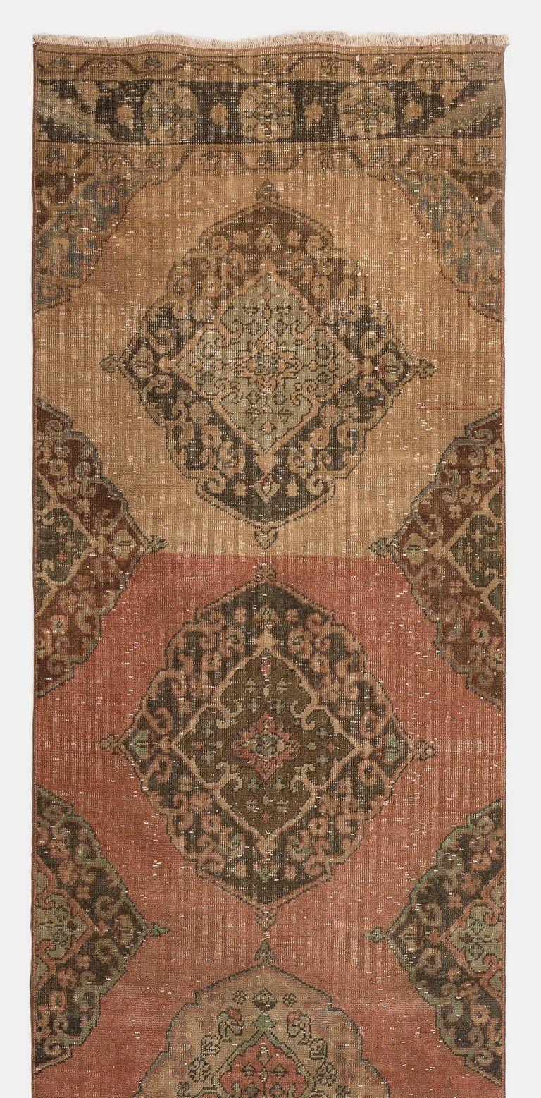 Esta alfombra turca vintage fue anudada a mano en la década de 1960. Presenta múltiples medallones enteros y medios medallones decorados con motivos florales en marrón, melocotón y verde salvia sobre un fondo liso en melocotón y coral oscuro. Tiene