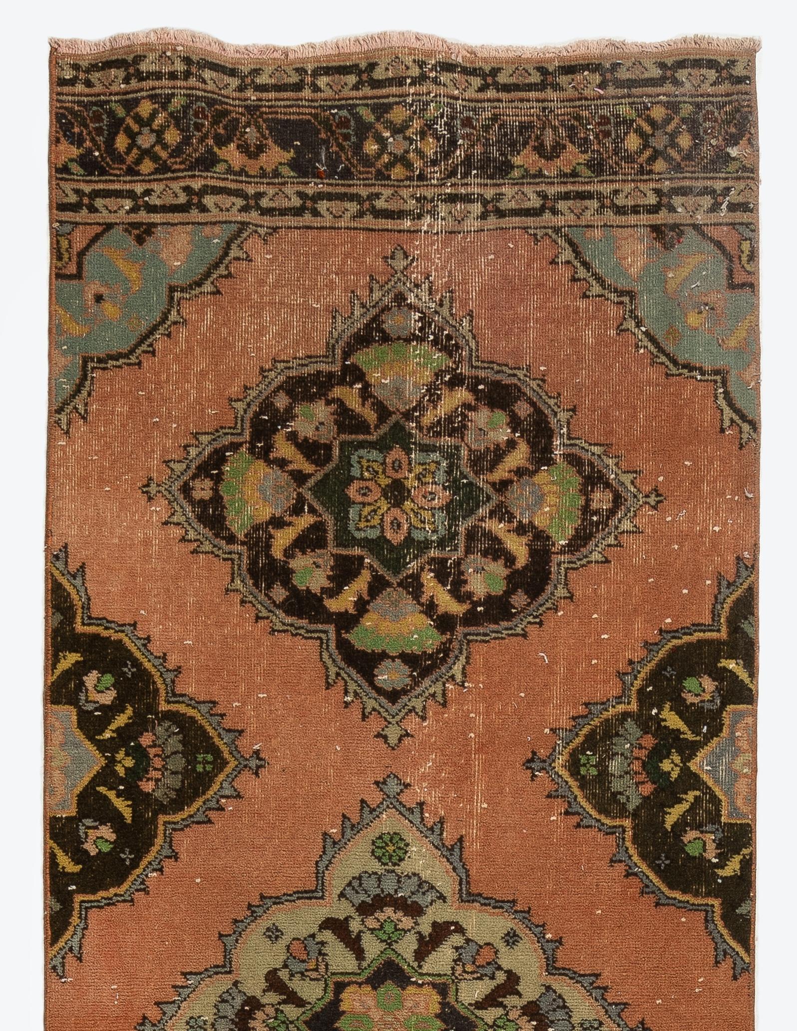 Una alfombra de pasillo vintage procedente de Turquía. Está hecha de pelo de lana medio sobre base de lana y presenta múltiples medallones enteros y medios decorados con motivos florales en marrón, verde claro, rosa salmón y azul pizarra sobre un