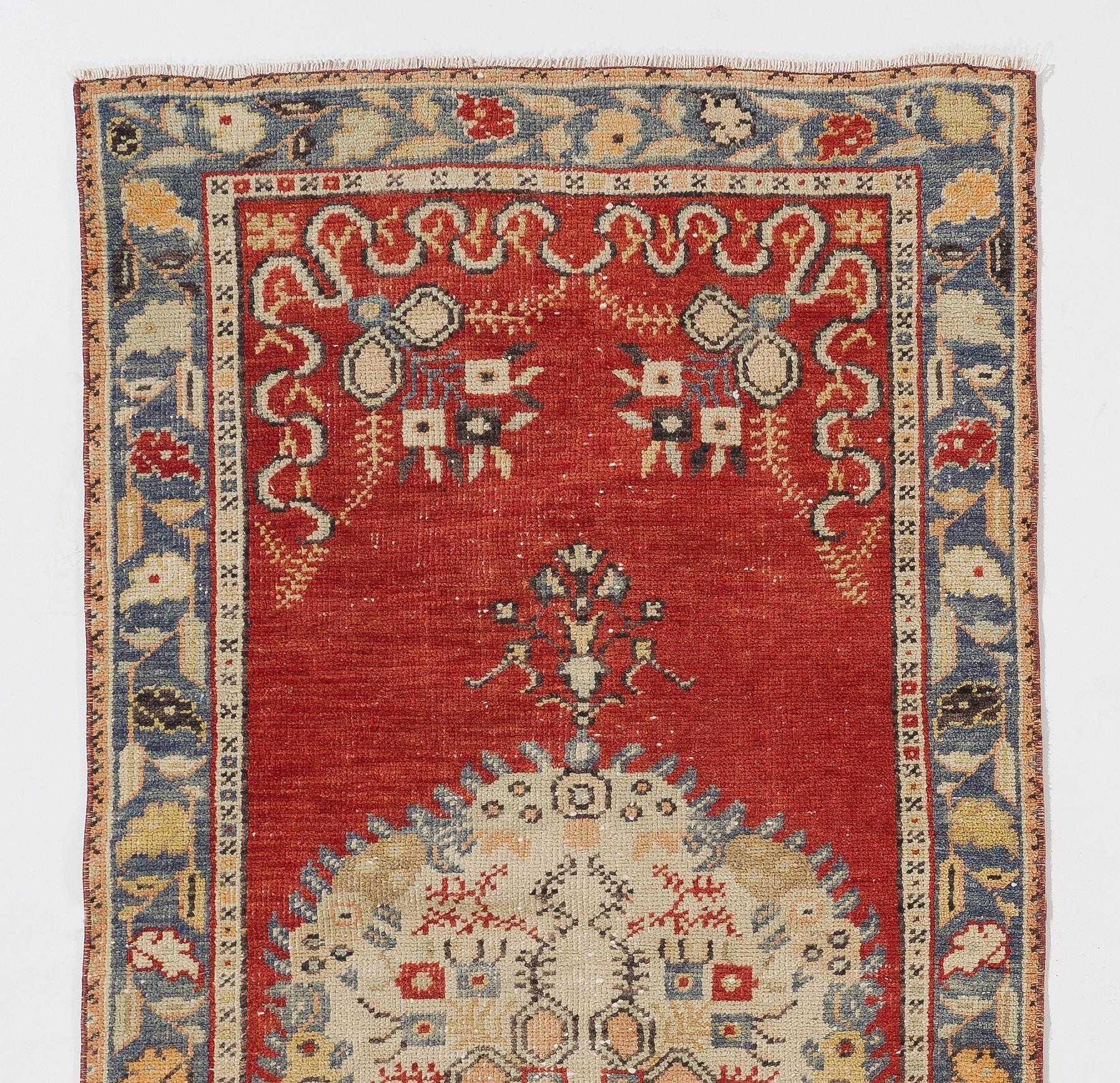 This vintage hand knotted accent rug from Central Anatolia has a large, elliptical medallion at its centre in ivory decorated with depictions of peacock feathers and stylized blossoms against a field in chilli red featuring bouquets of flowers on