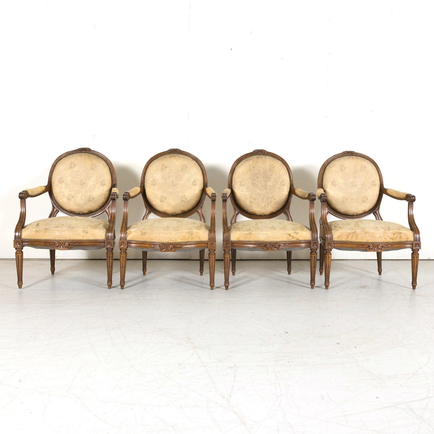 Four stunning 19th century French Louis XVI style armchairs, expertly handcrafted of walnut near Lyon, circa 1890s. Each elegant fauteuil à la reine features a classic padded medallion back crowned with a finely carved rose crest, gracefully