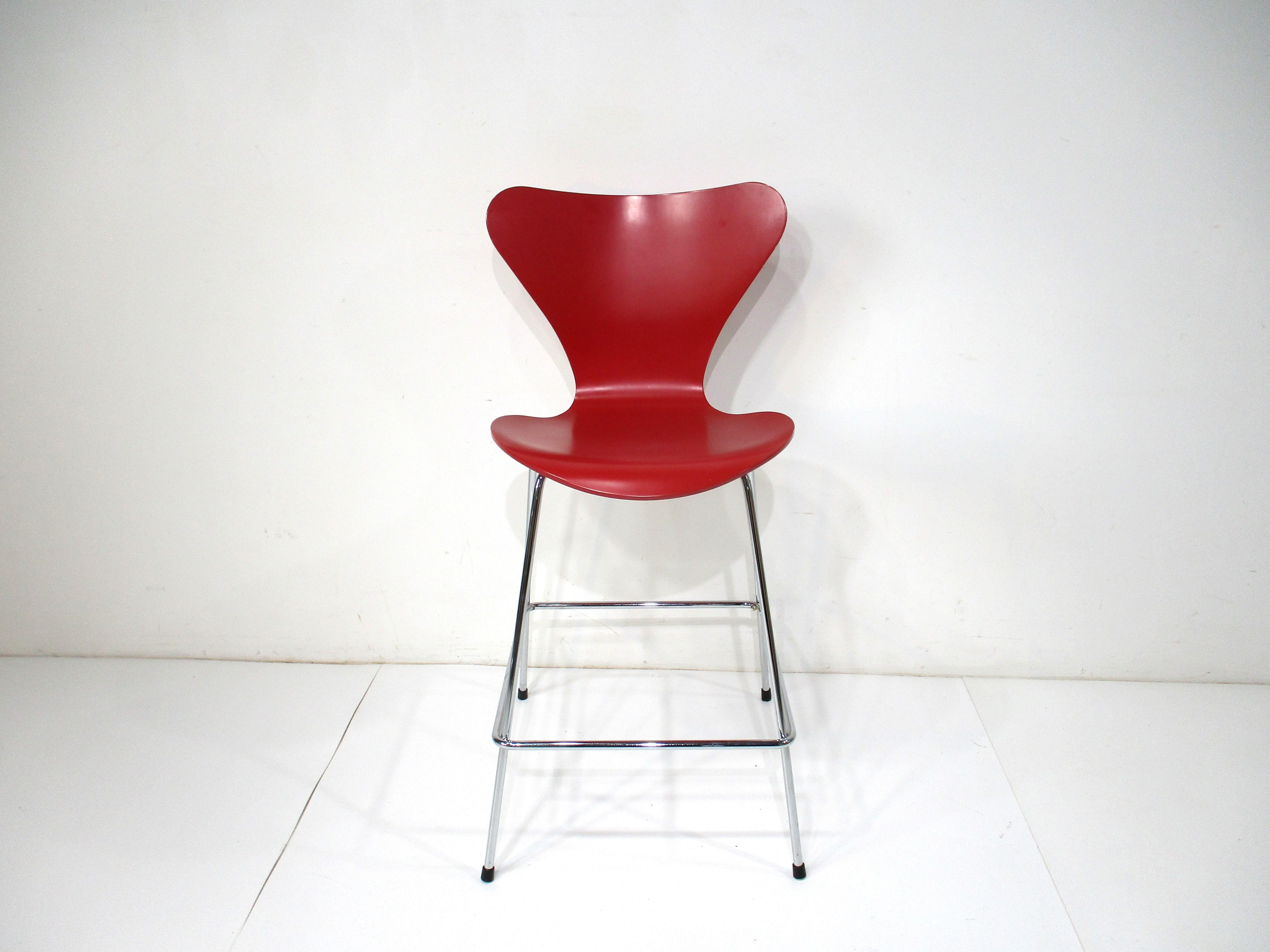 A set of four counter stools having red molded plywood seats on chromed metal frames with rubber foot pads to protect your floors . These bar / counter stools have foot rests to the lower frame for comfort . Designed by Arne Jacobsen and