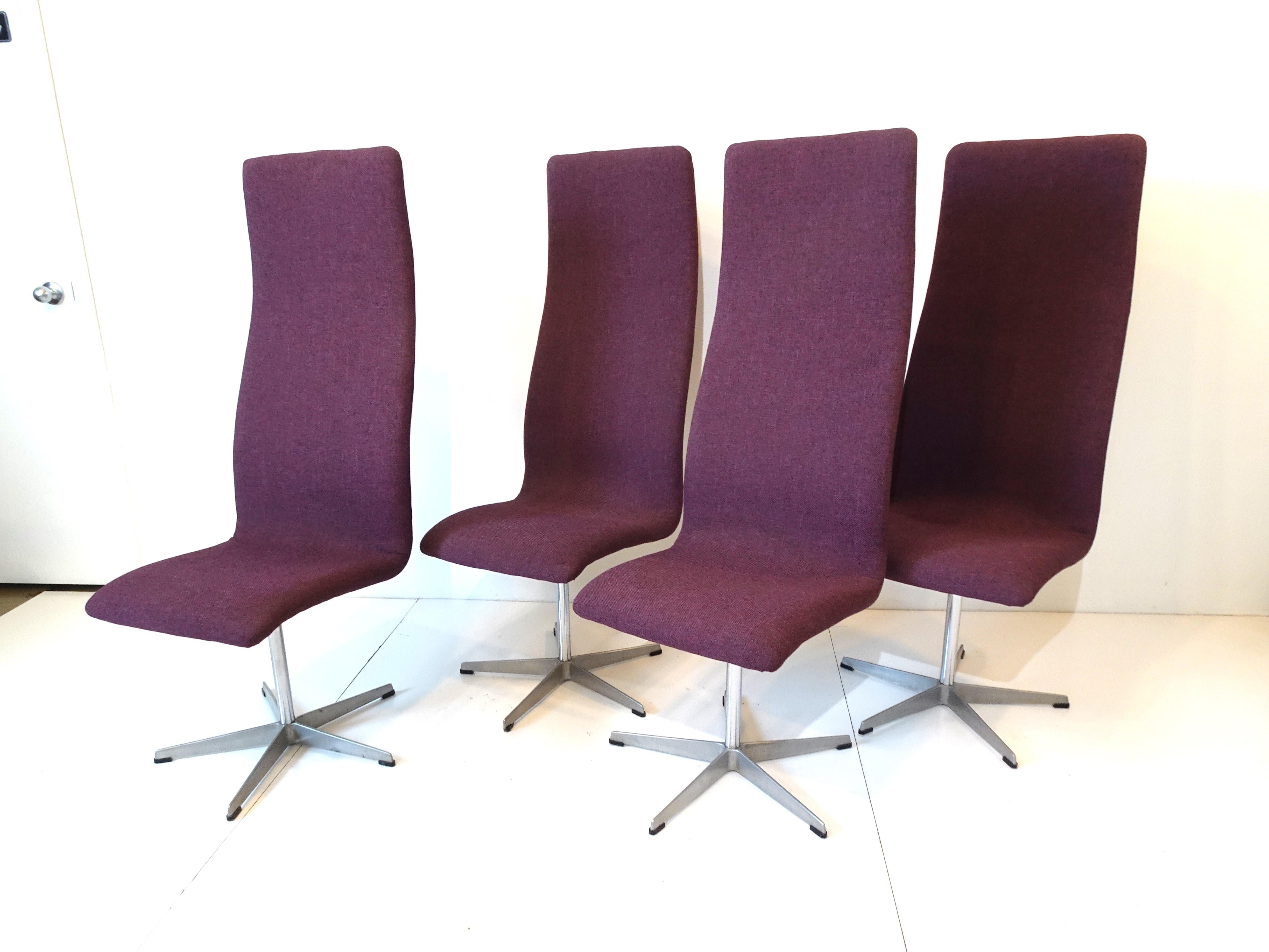 A set of four swiveling upholstered Oxford dining chairs in a tightly woven dark purple contract fabric with chromed shaft and cast aluminum star base having plastic feet to protect your floors . Model number 7403 manufactured by Fritz Hansen made