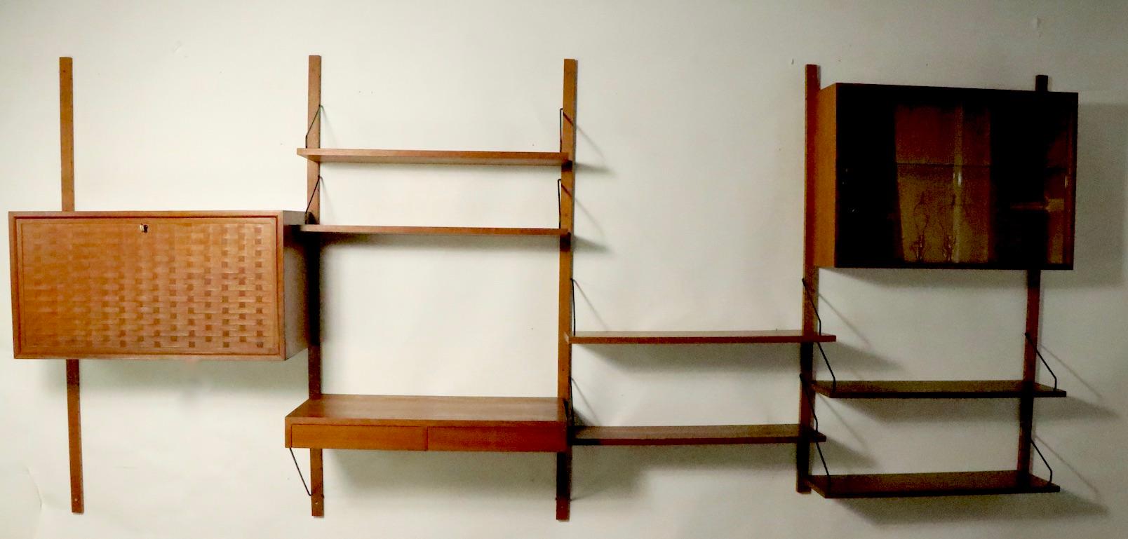 Nice Danish Mid-Century Modern wall unit designed by Poul Cadovius. The set consists of 4 vertical supports, ( 1 ) Woven drop front locking, light up, cabinet ( 31.5 W x 15 D x 17 H ). ( 1 ) 2 drawer writing desk ( 31.5 W x 16 D ). ( 1 ) Glass front