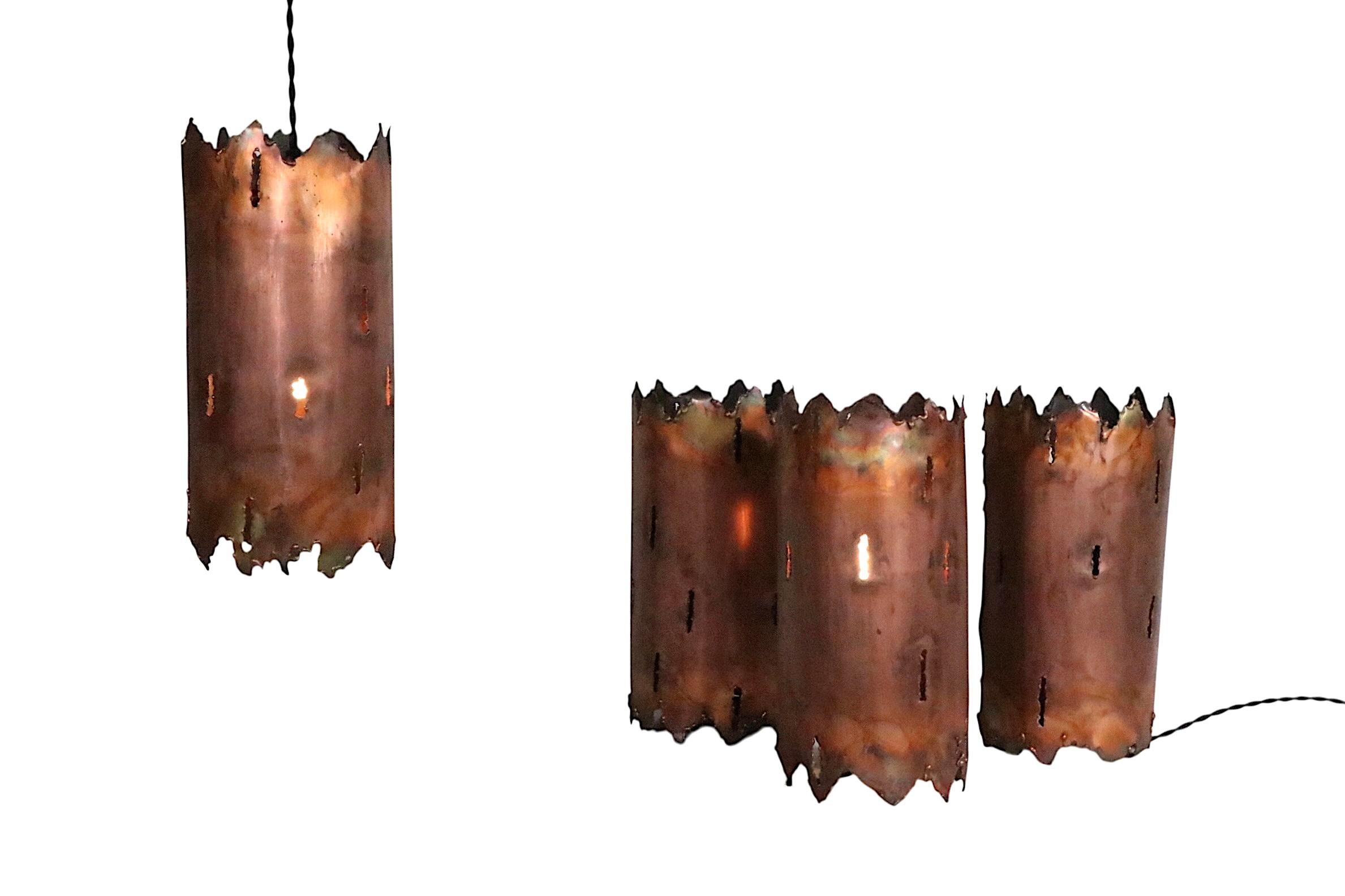  4 Brutalist  cylindrical torch cut copper light fixtures, attributed to Tom Greene, circa 1970's.
 These fixtures are cleverly designed to function either as hanging pendant lights, or flip them over and function as table lamps. The lamps have been
