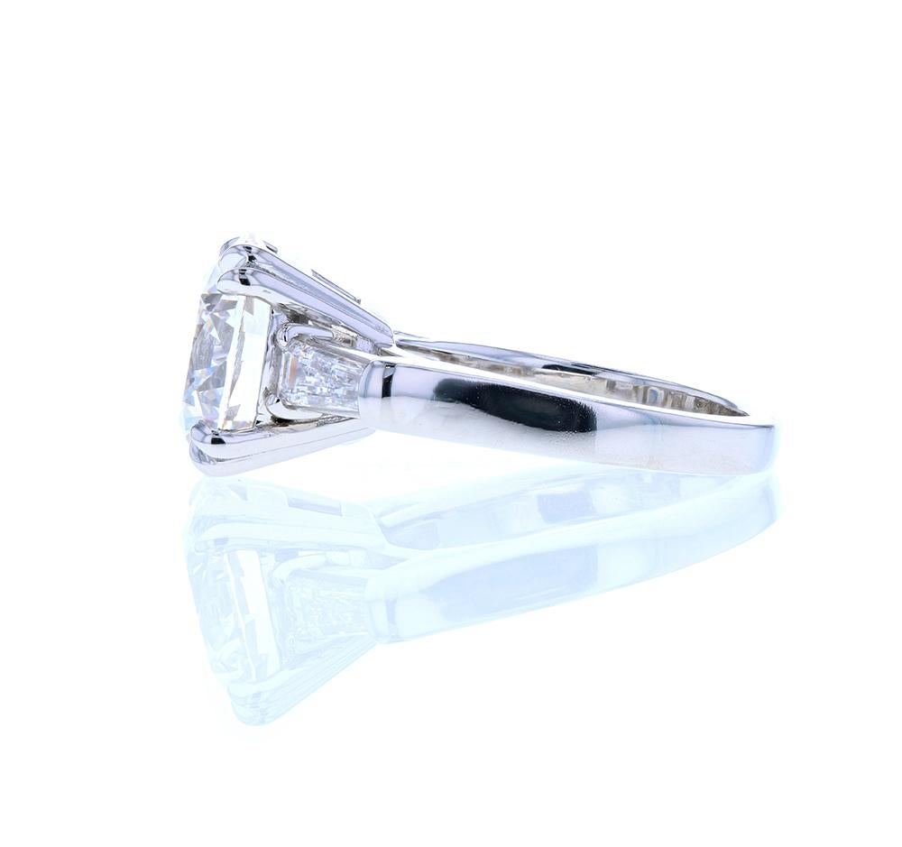 This stunning four carat diamond engagement ring with diamond baguettes on the side is a sight to behold. With an elegant three stone platinum setting with a raised profile and double eagle claw prongs, this four carat, E color VS1 GIA round diamond